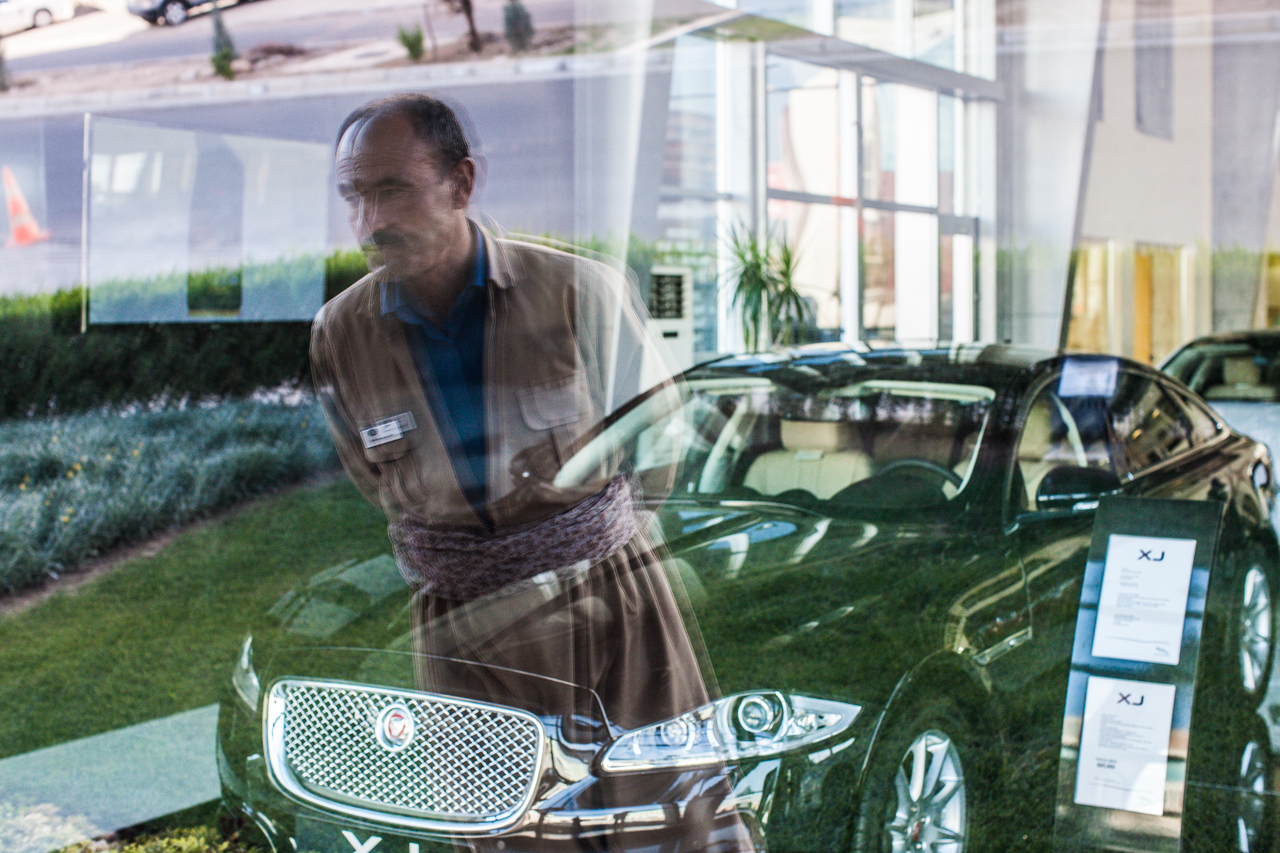 A Kurdish man in traditional clothes looks through the window of the new Jaguar dealership he guards in Erbil.