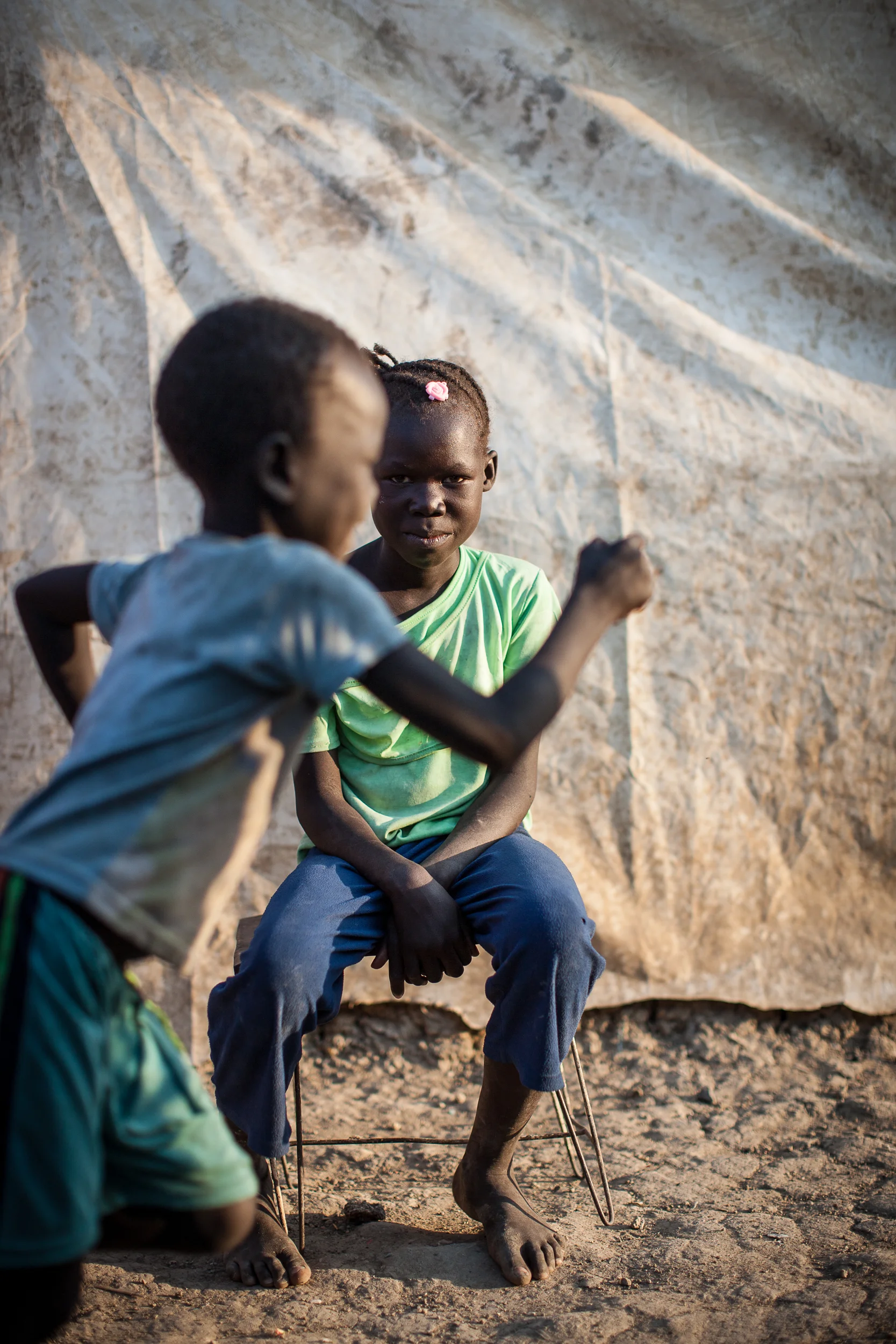 A young boy runs past Anit, 8. Anit and her family of 5 all ran from Malakal when fighting descended on the town. She now lives in the PoC site on the UN's Malakal base.