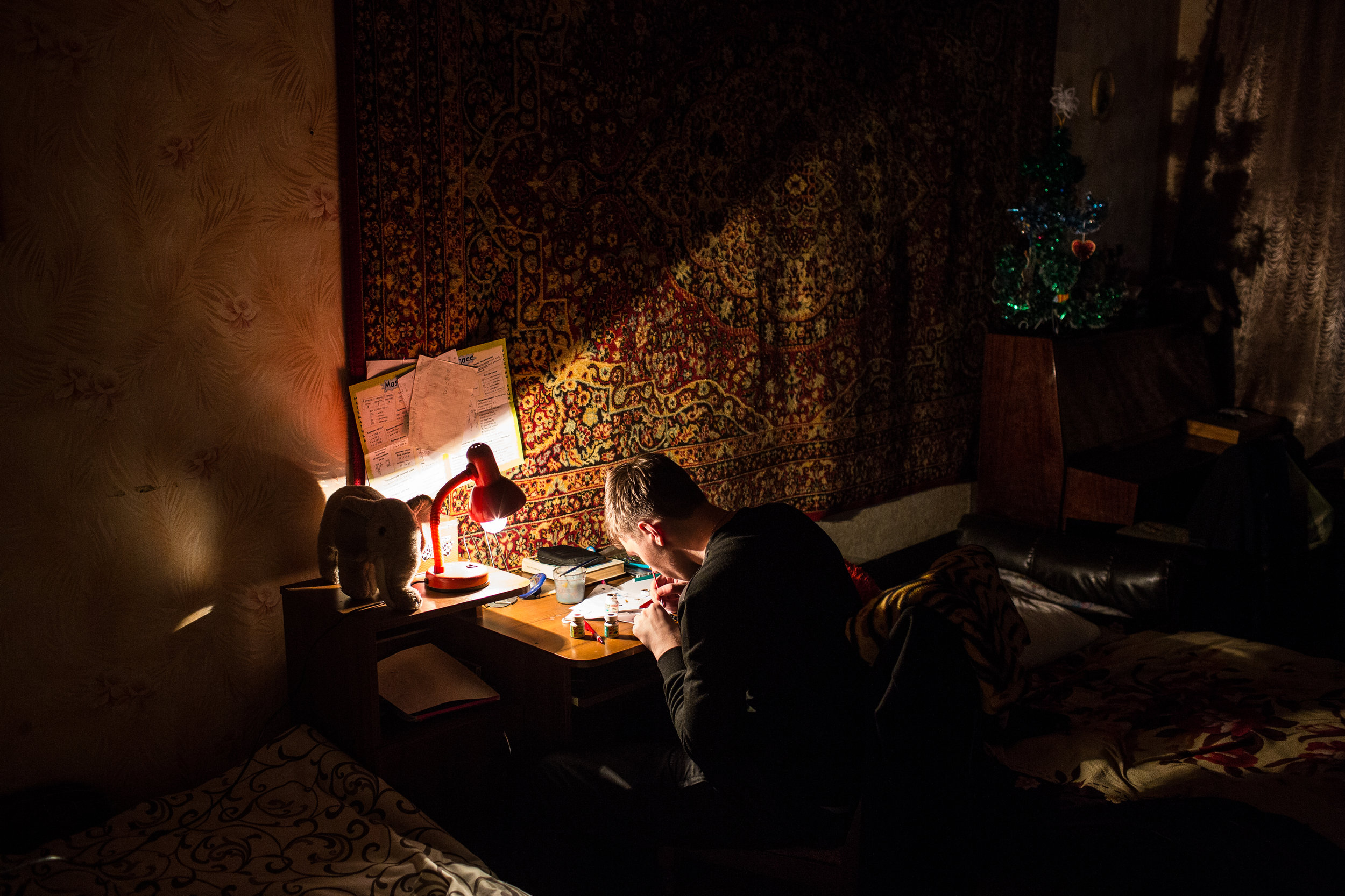 Kostya paints small model figurines at the apartment. "I live day by day," he says while sitting at his desk one night, "I don't look into the future because your plans usually don't come true."