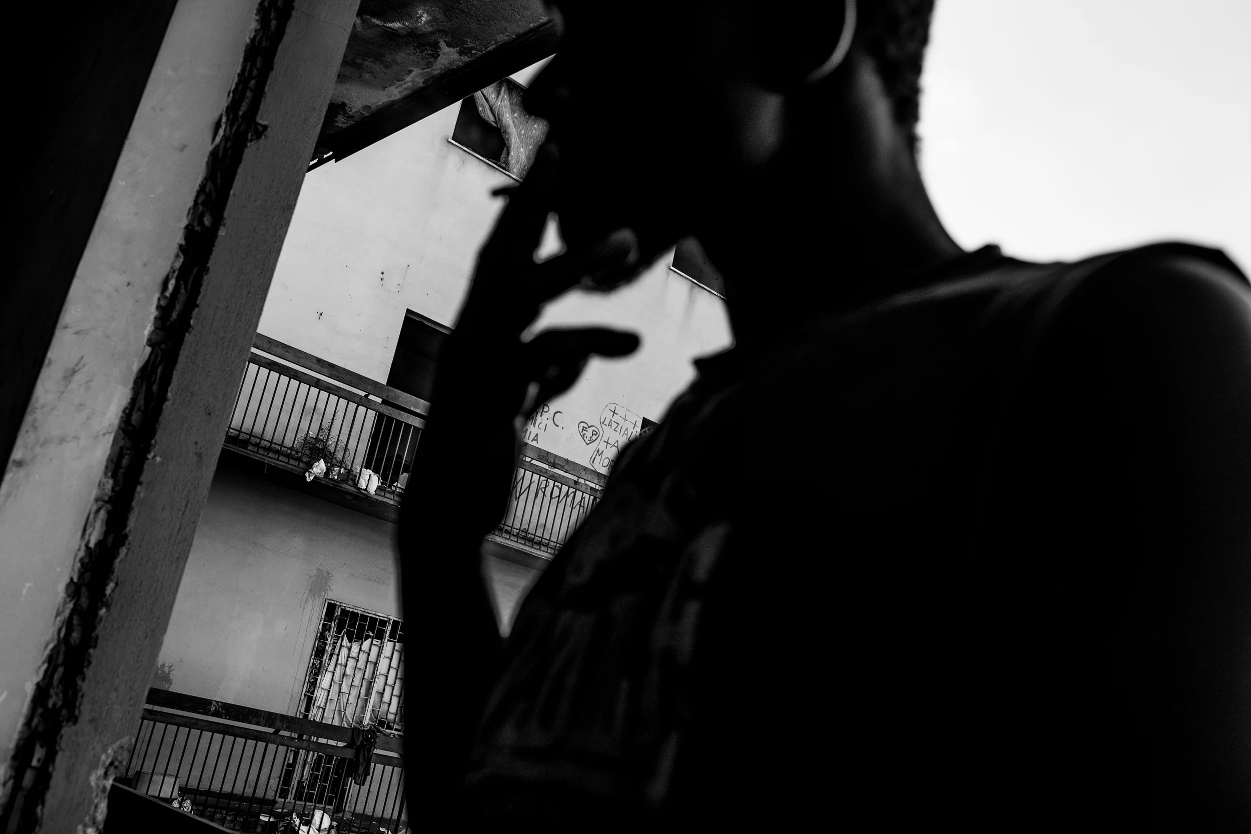 A migrant smokes a cigarette in the abandoned factory where he lives. "I never smoked at home because it's unhealthy," he sighs, "but it helps my hunger and the stress. Life here is short."