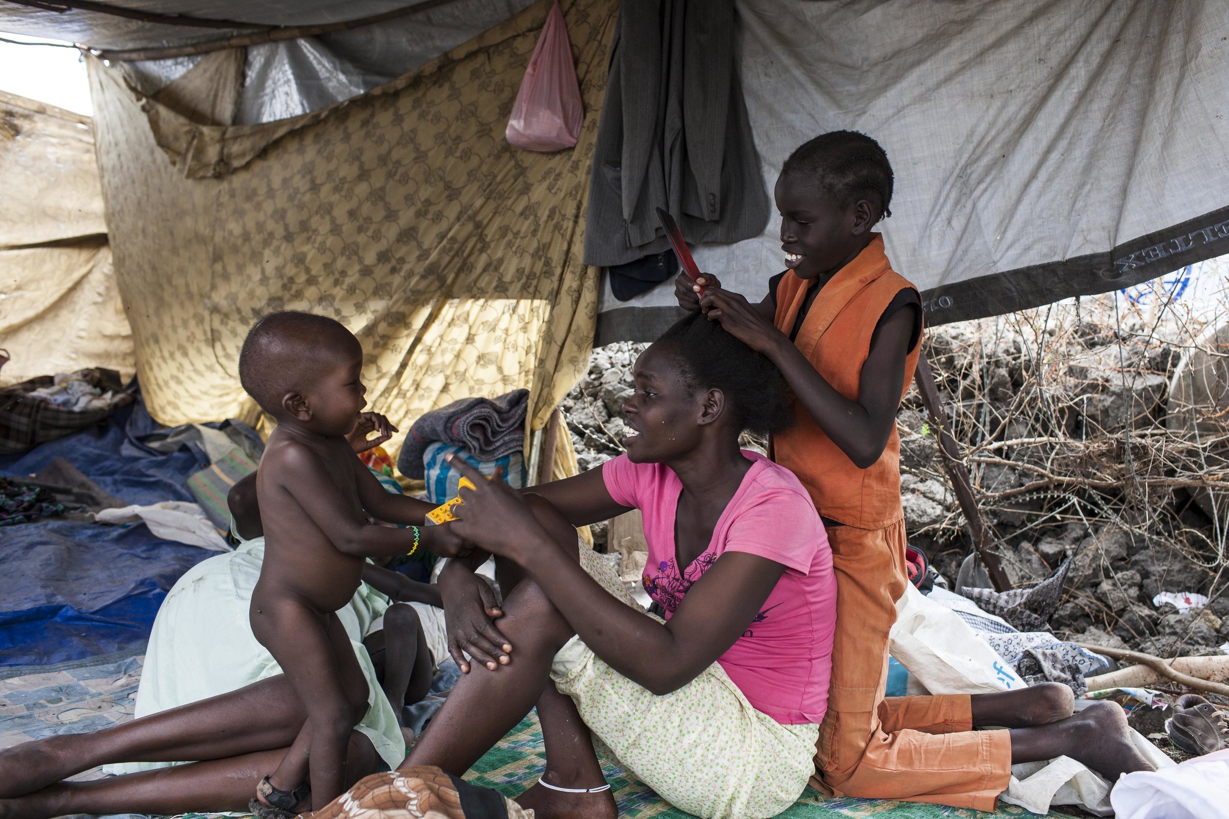  Bor, right, combs Regina's hair as Regina tells her son, Anuen to get ready to leave for the bus. "We are staying like small children here [in UNMISS]. It is no life," laments Kuany, "There is no food and when the rains come it will be more bad and 