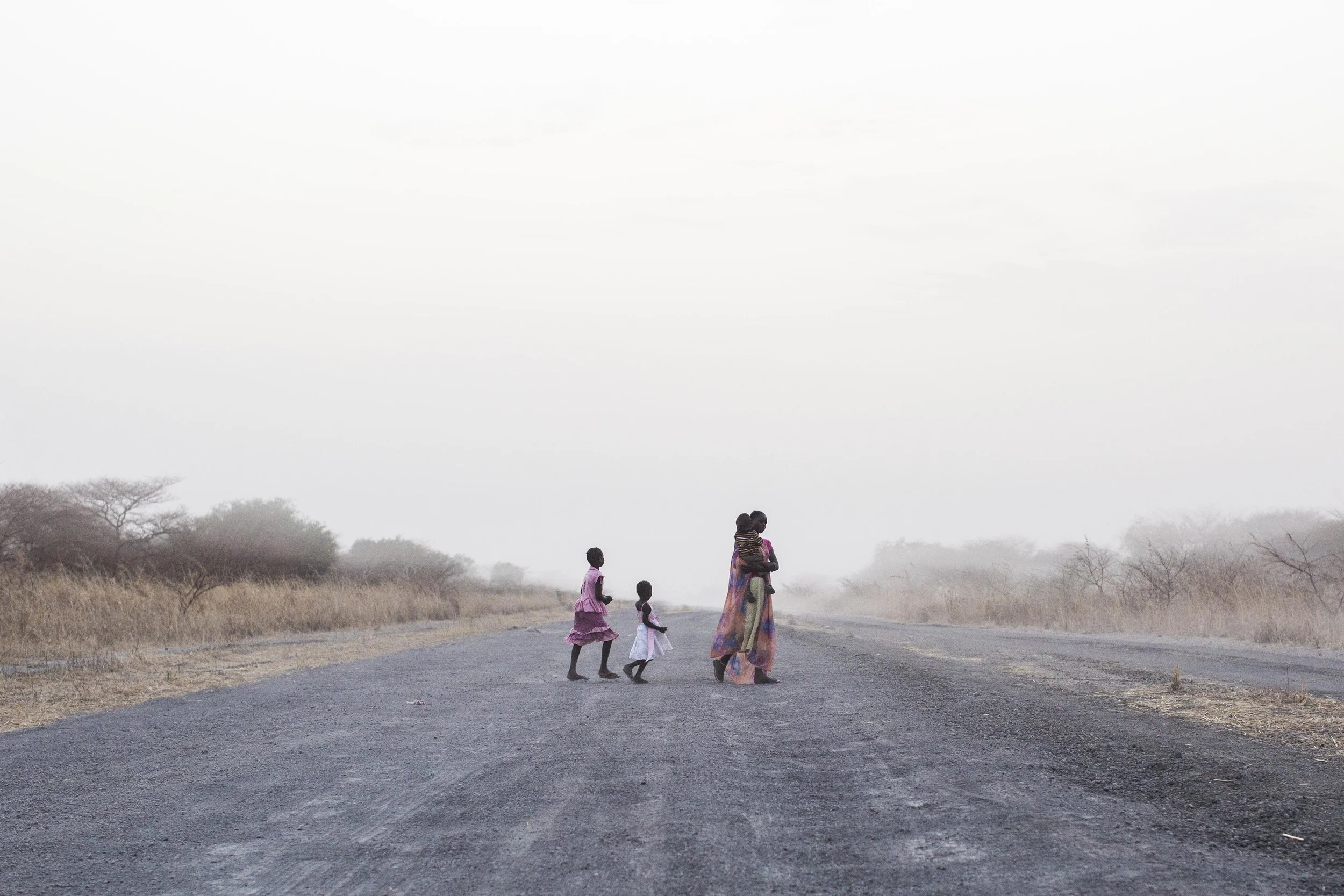  Regina carries Anuen and walks with Adut and Akon along the road after the sun sets. "I must return them [his children] to school," worries Kuany, "if they are having no school there will be nothing for them." According to the World Bank 73% of thos