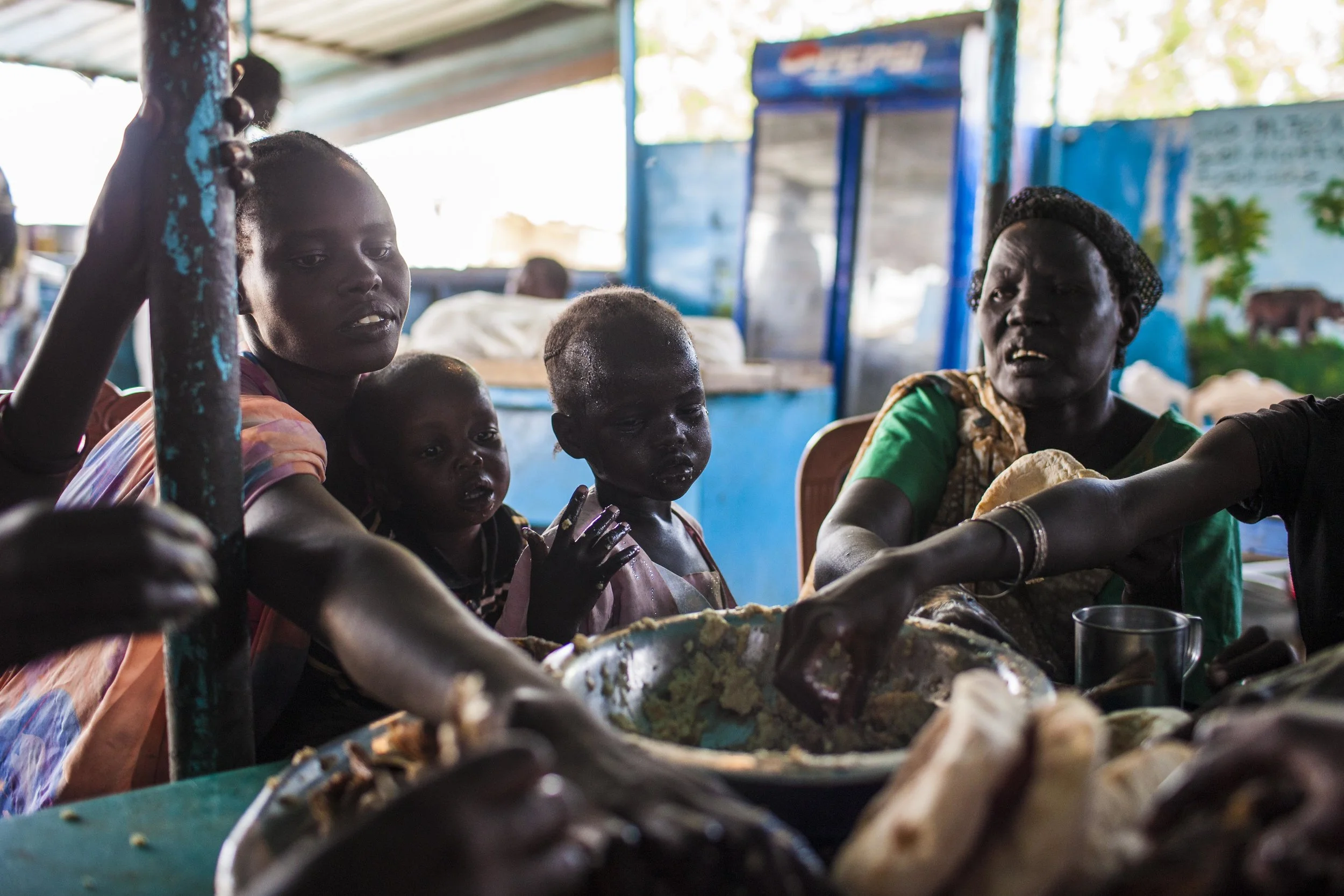 Regina, Anuen, and Adut dig into a bowl of beans and bread at a small village along the road to Renk the following day. Only a few hours from Renk, it is their first real meal since leaving Malakal three days before.