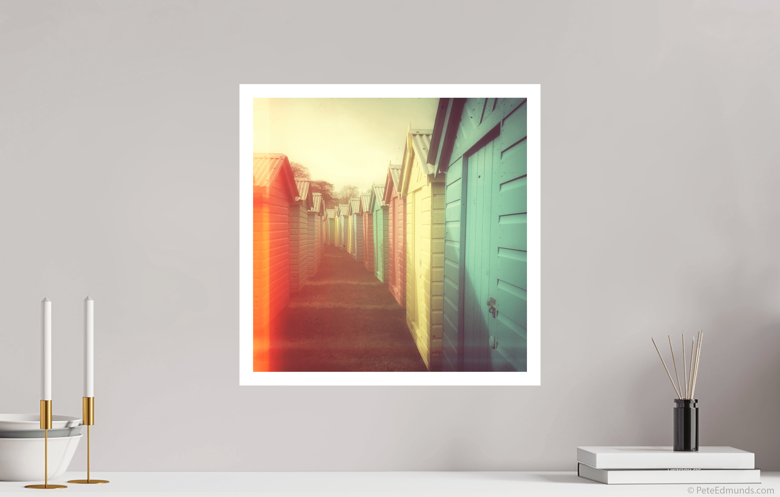 Fine art print Beach Huts 01B-Retro by Pete Edmunds, 40 × 40 cm with 2 cm white border, shown above a white sideboard in a modern interior.