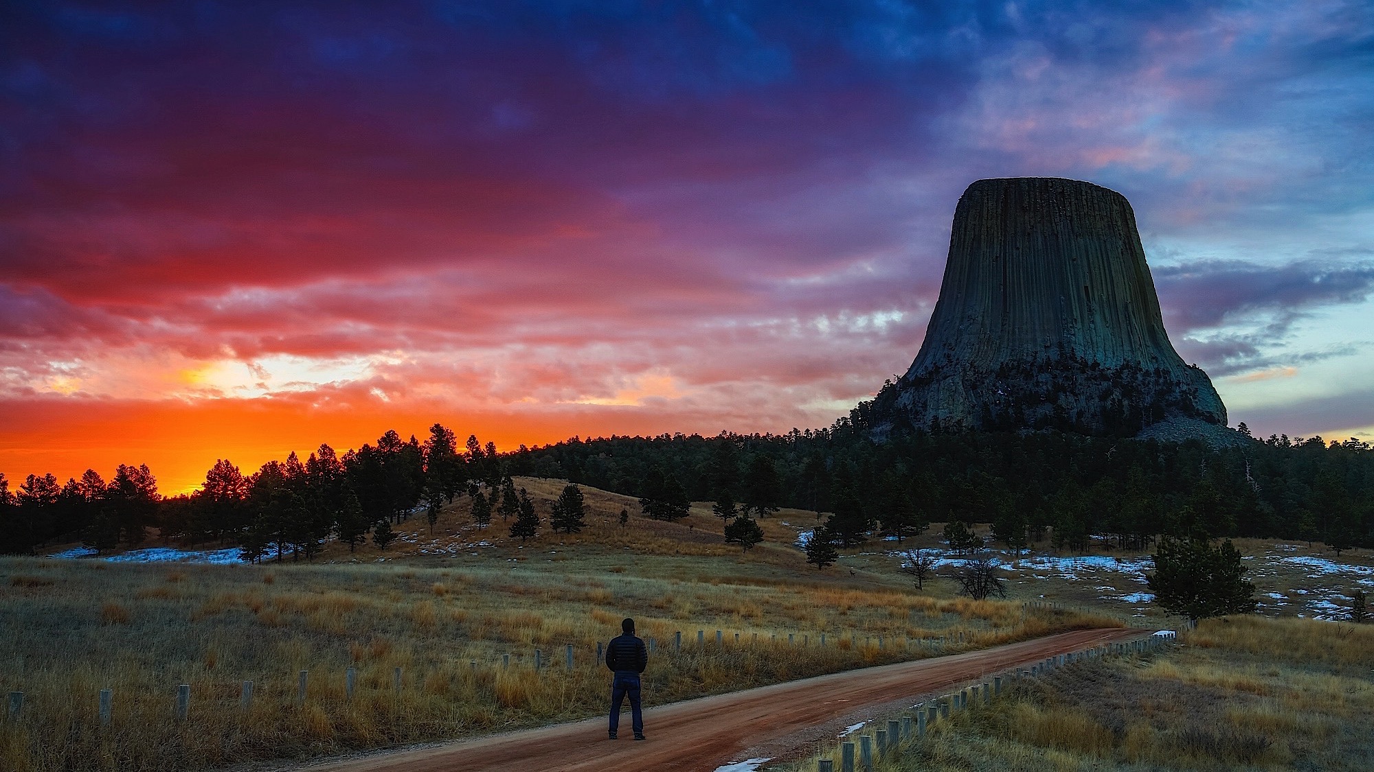 a lone hiker enjoys a dramtic sunrise over Devils tower national monument, WY
