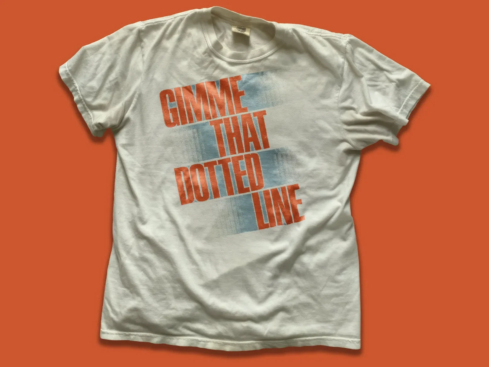 White T-shirt with orange and blue text that reads 'GIMME THAT DOTTED LINE' on a solid orange background.