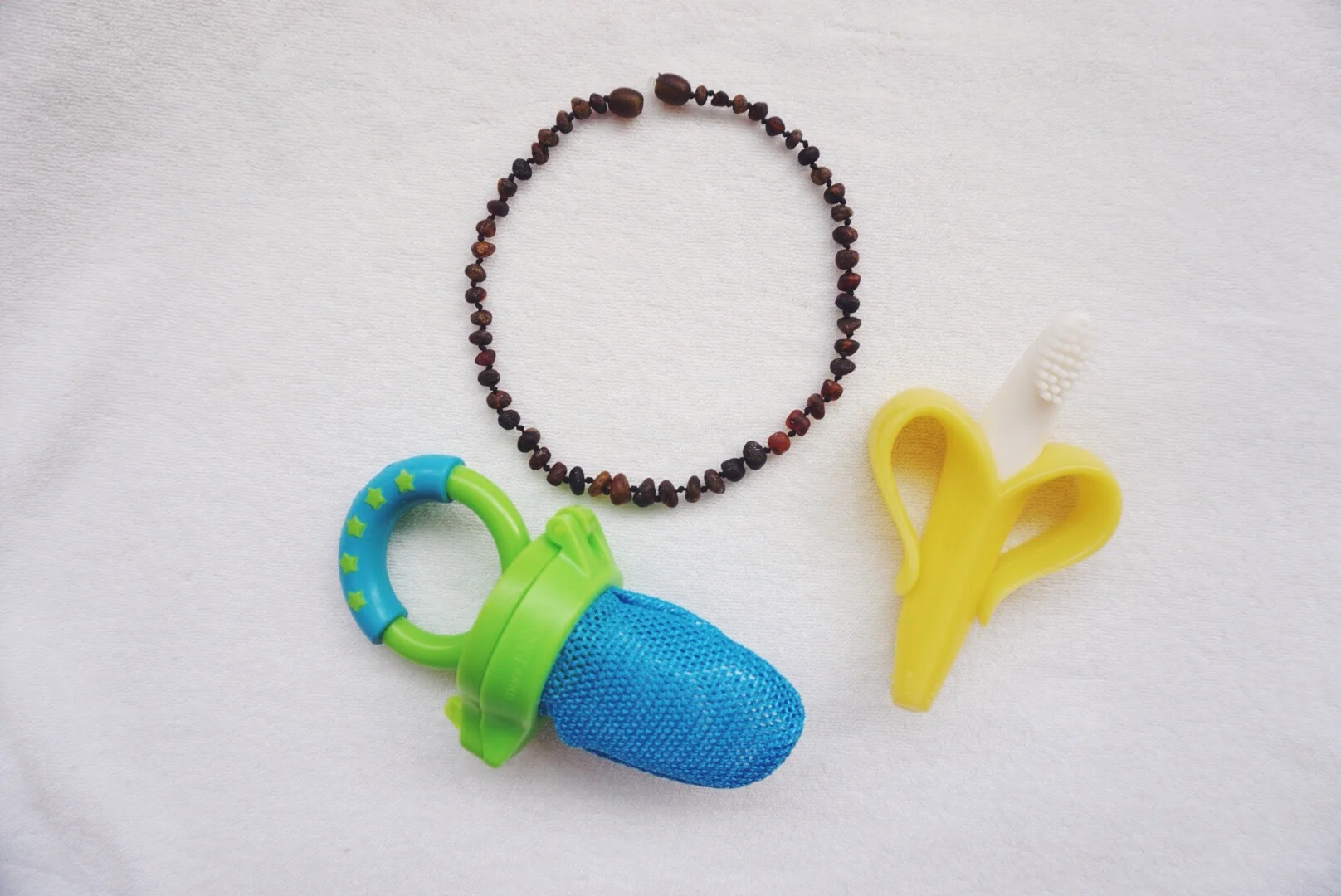 (clockwise) Amber teething necklace, Baby Banana Infant Teething Toothbrush, Munchkin Fresh Food Feeder. 