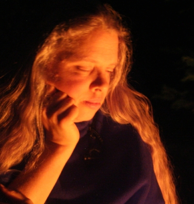 Image of Arie Farnam with long light-colored hair unbound and eyes closed as she looks into a fire at night