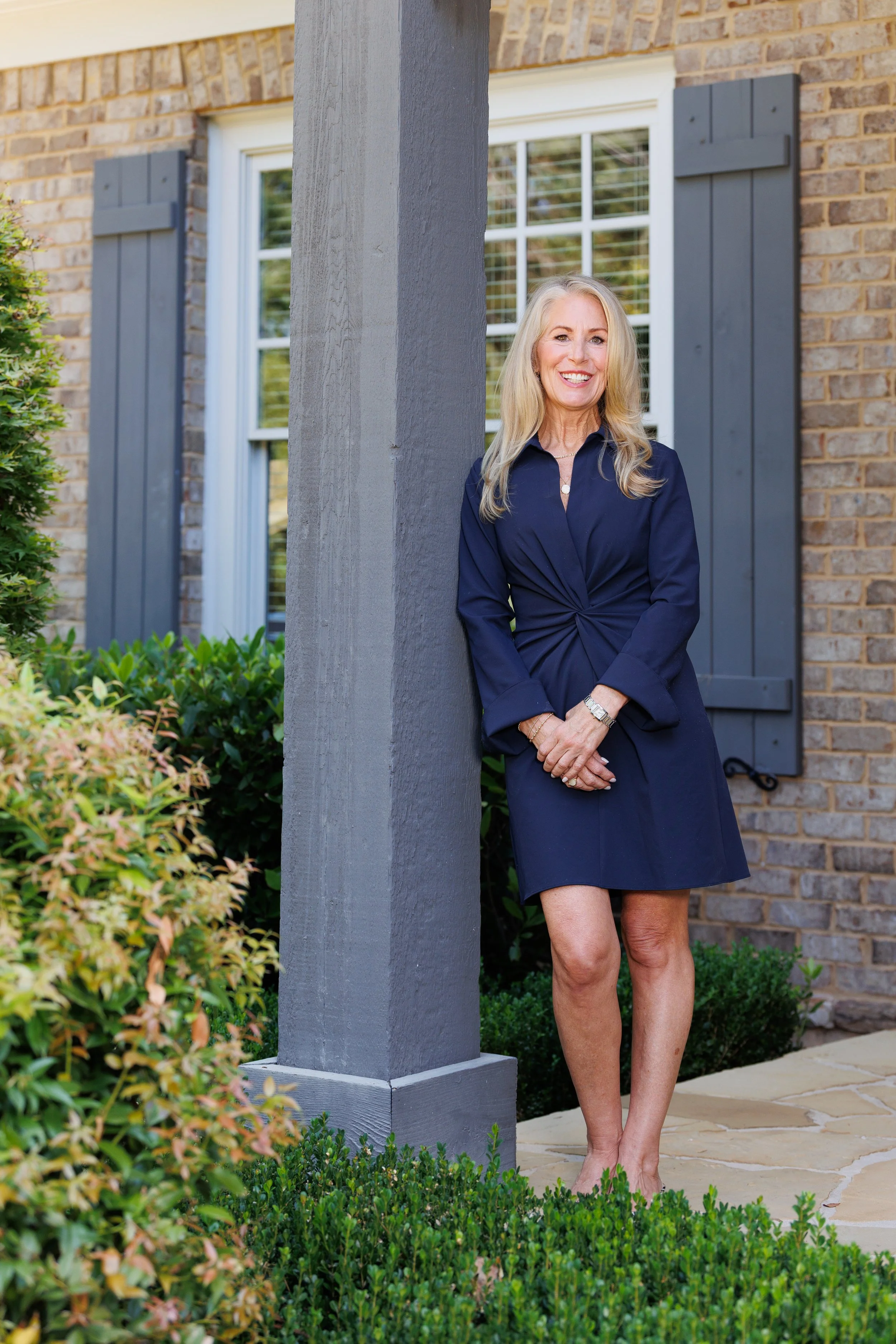 Professional headshot of real estate agent Shannon Inhouse smiling in front of a nice brick home, captured by CatMax Photography.