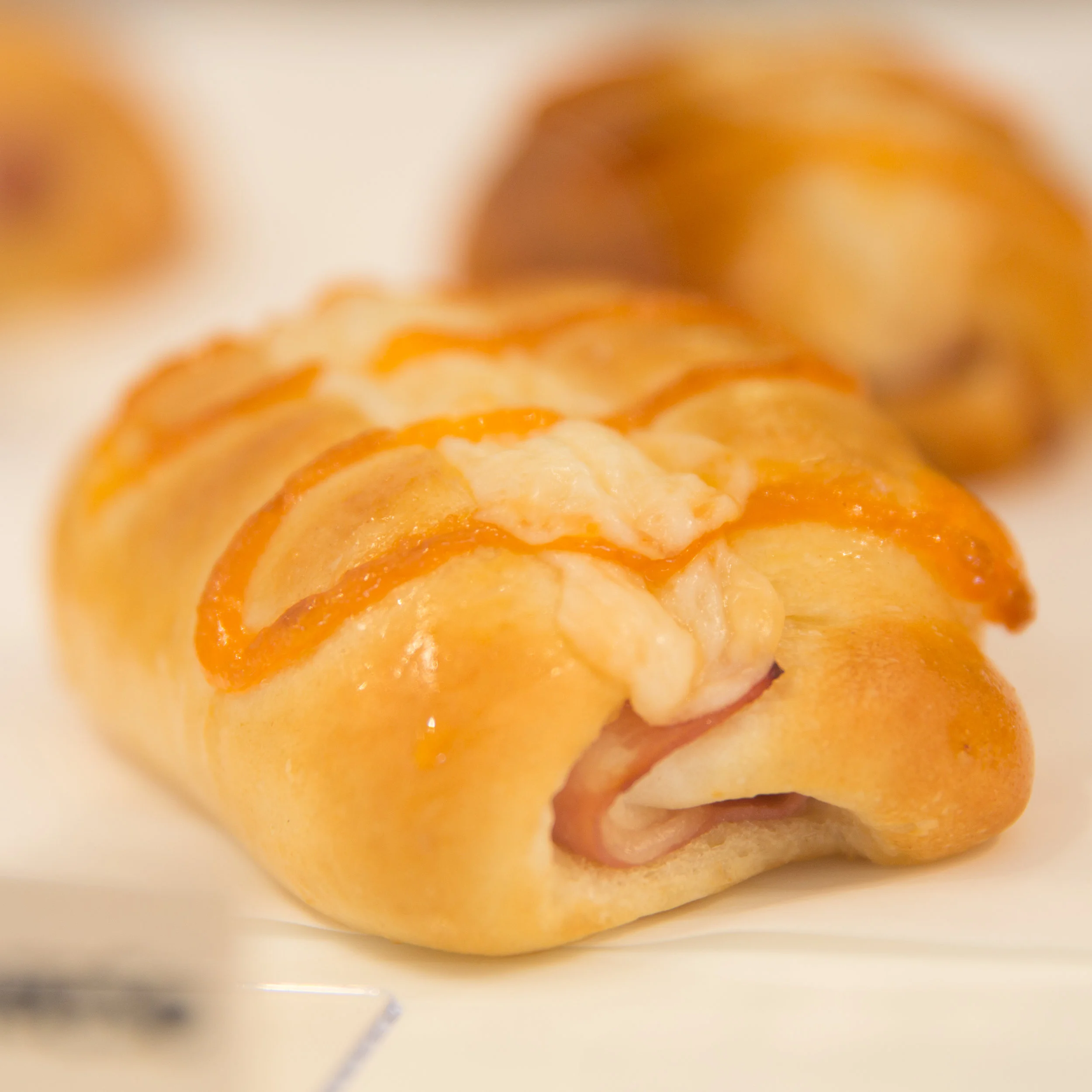 Ham & Cheese Bun Inspired by our neighbor's suggestion, we created the Ham & Cheese Bun with Mozzarella cheese in the filling, Parmesan cheese as topping, drizzled with homemade Sriracha Aioli dressing. With carefully picked lean ham, this is the perfect savory item.