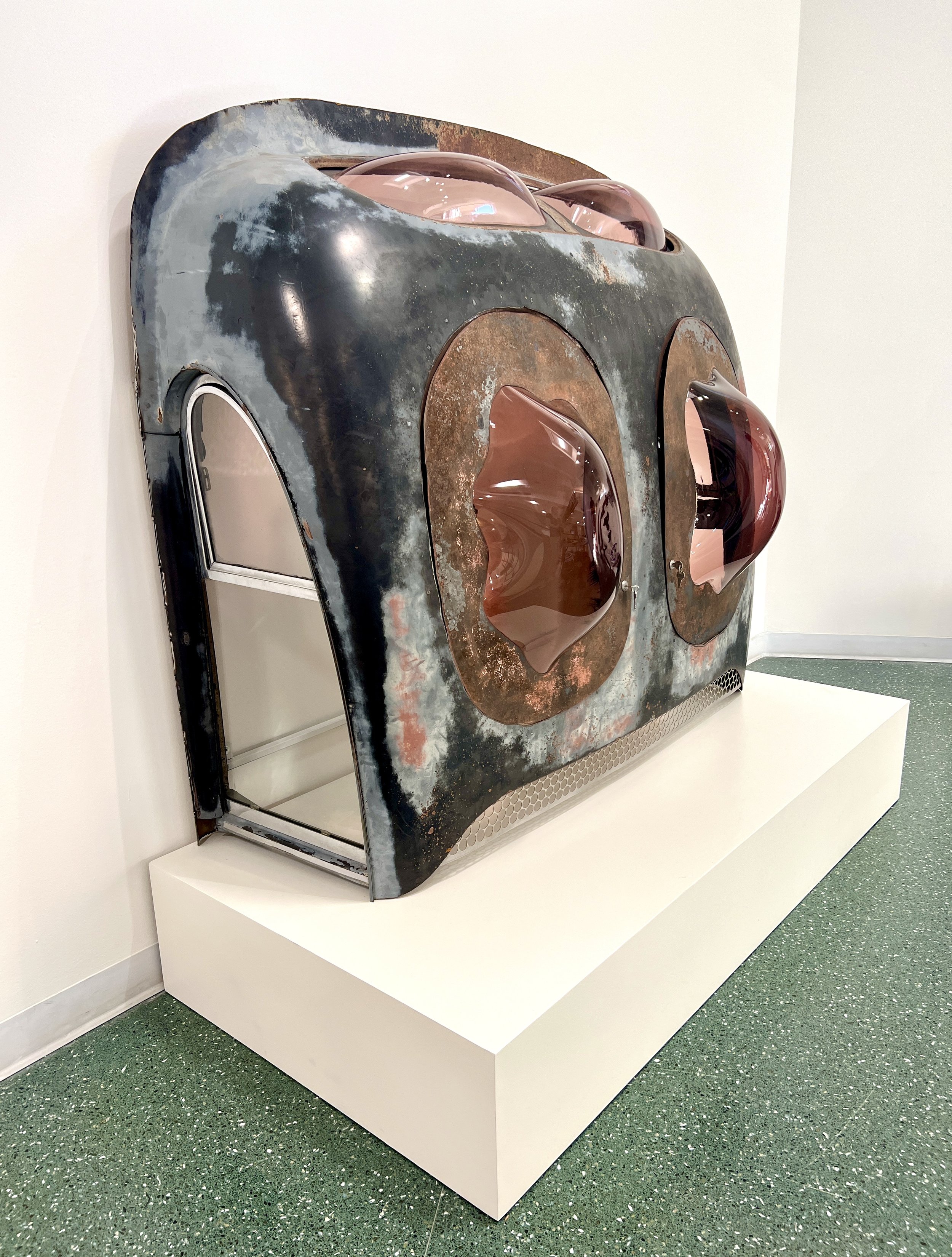 This “car cabinet” was made from the roof of the car, using the massive door hinges of the car to create functional doors with kiln-formed glass windows. Glass also bubbles up out of the former rear window.