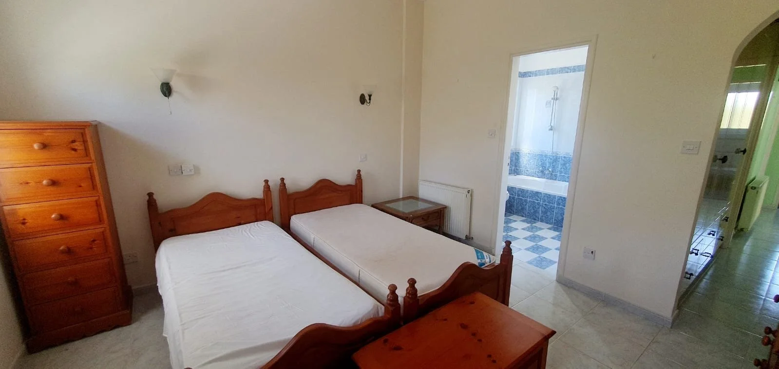 Bedroom with two wooden beds, a chest of drawers, a nightstand, and an open bathroom door showing a bathtub and shower.