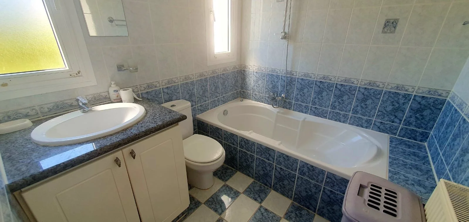 Bathroom with a sink, toilet, bathtub, and tiled walls and floor, with a window letting in natural light.