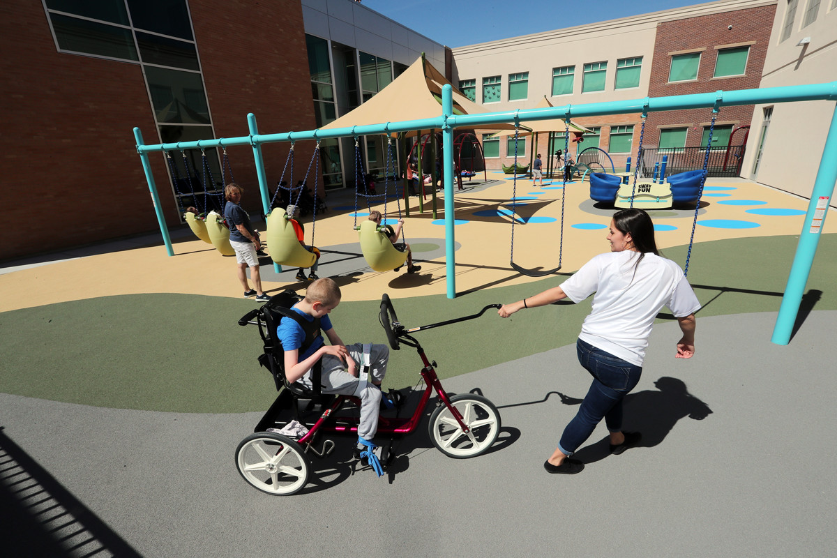 Christian Knudson rides a bike with the help of Angel Randles as students at the Kauri Sue Hamilton School in Riverton enjoy their new playground on Tuesday, May 14, 2019. - Scott G Winterton, Deseret News