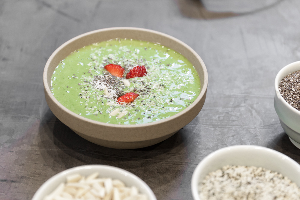 A matcha smoothie bowl with chia seeds, strawberries, cashews, and coconut shavings. 