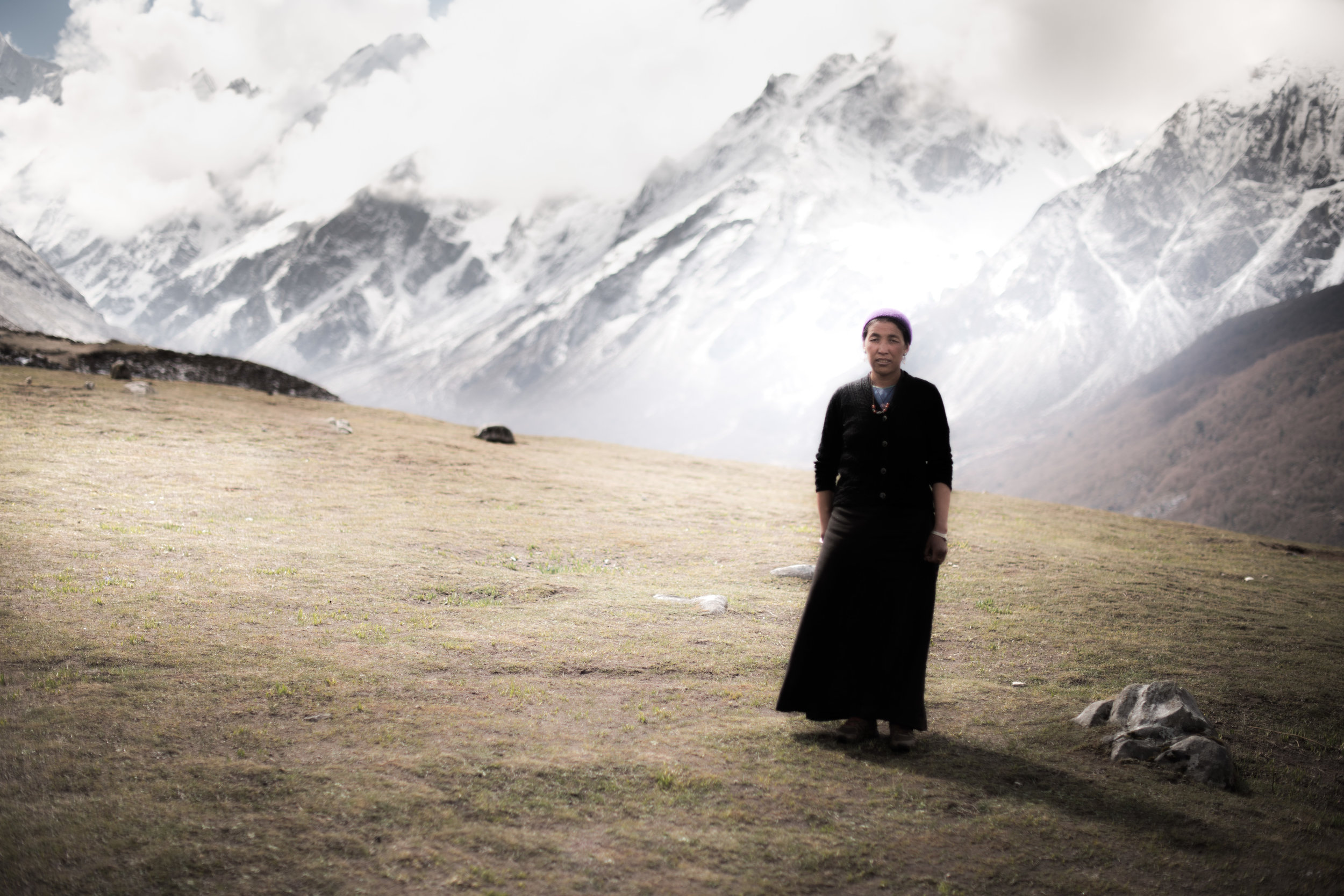   On the outskirts of Kyanjim Gumba stands Cheoten Lama. Behind are the Himalayas, the source of the avalanches that struck her village.&nbsp;  Cheoten has a full time job feeding the workers rebuilding and expanding the town.  