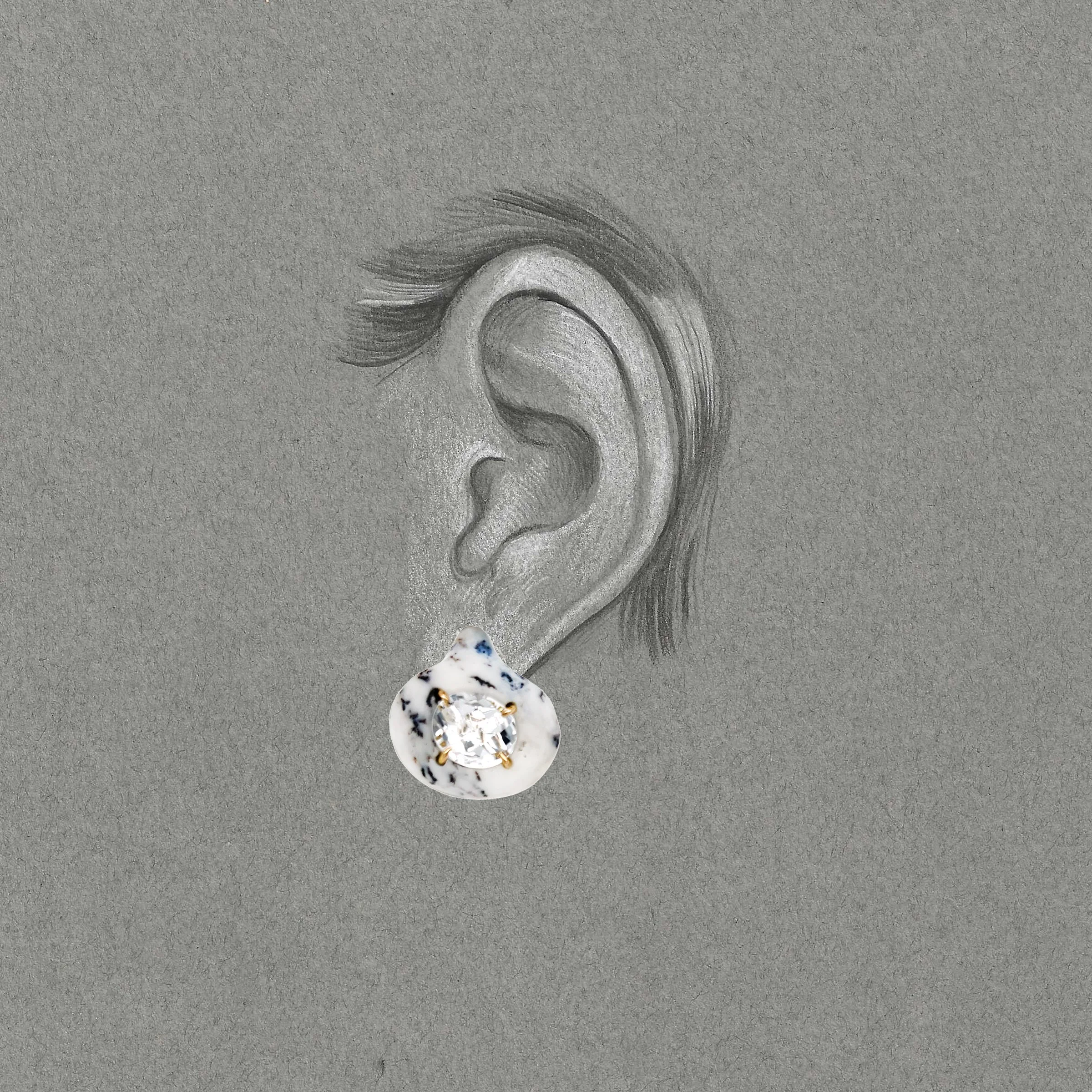 White tear drop shaped earrings placed on a grey drawing of an ear.