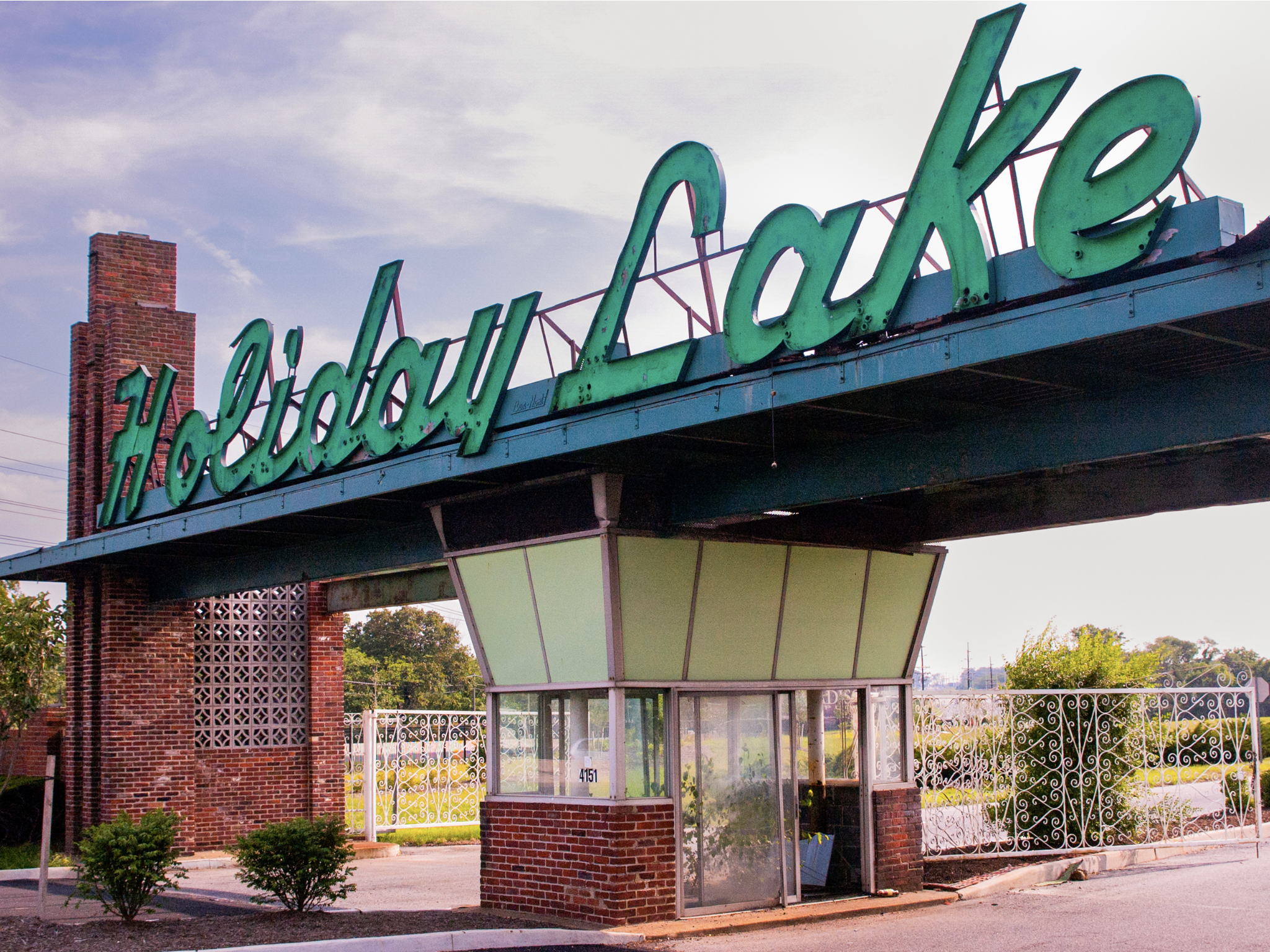 A vintage-style sign reads 'Hidalgo' in large, cursive, teal-colored letters mounted on a building with a brick chimney and decorative brick and metal fences in the background.