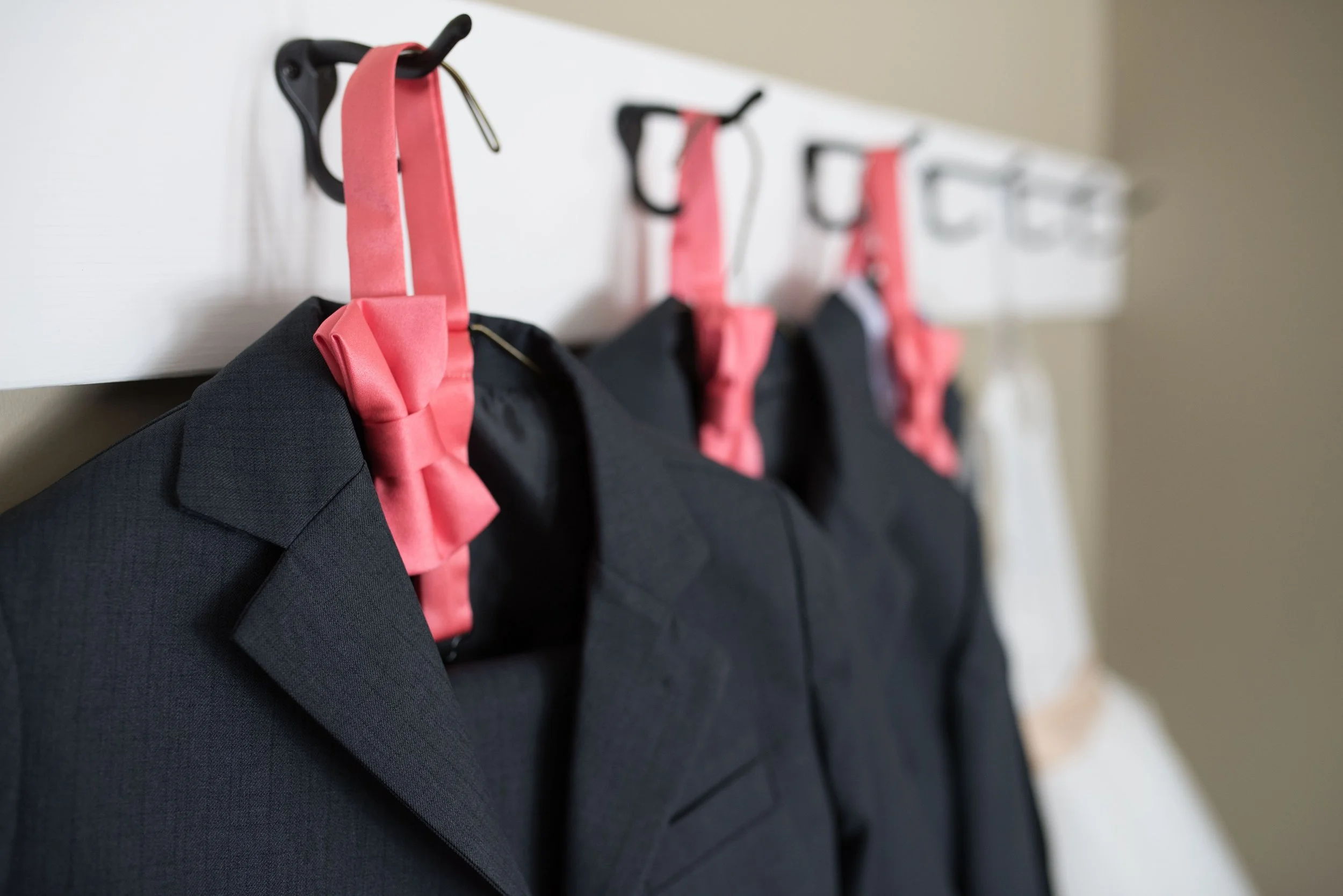Line of black suits with pink bows hanging on hooks inside a room.