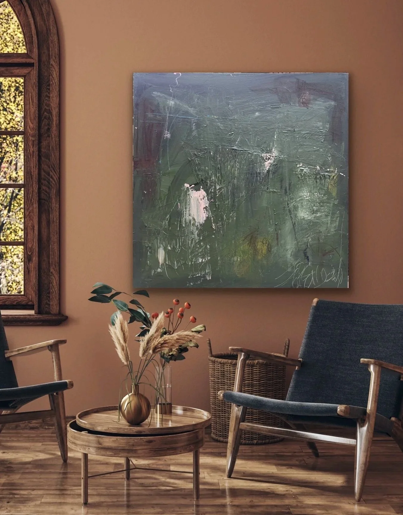 A cozy interior with a round wooden coffee table, beige walls, and a large abstract painting. There's a window with wood trim on the left, plants on the table, and seating including a modern armchair and a woven chair.