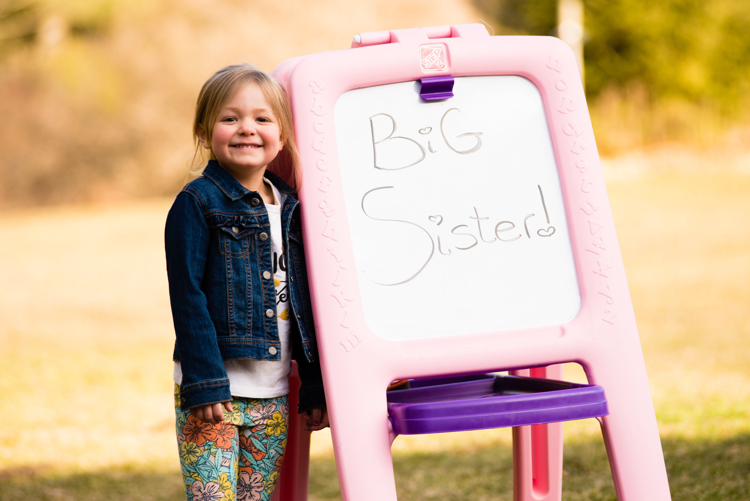 Young Girl Standing Next To "Big Sister" Sign