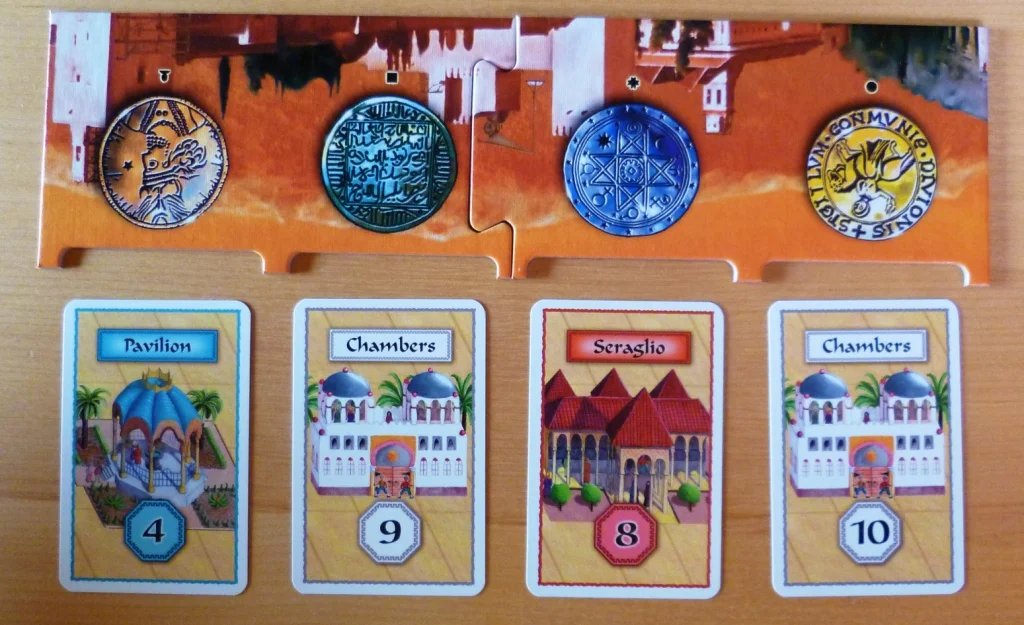 The board shows the currencies, the cards are the buildings, e.g. the White building on the right needs at least 10 yellow to purchase it.
