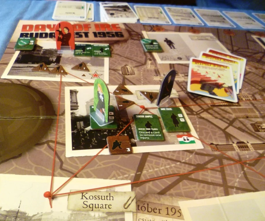 The photos on the board are locations in Budapest, the red lines depict routes, the standees are the revolutionary players, green are revolutionist characters and the brown pieces are SPA forces.