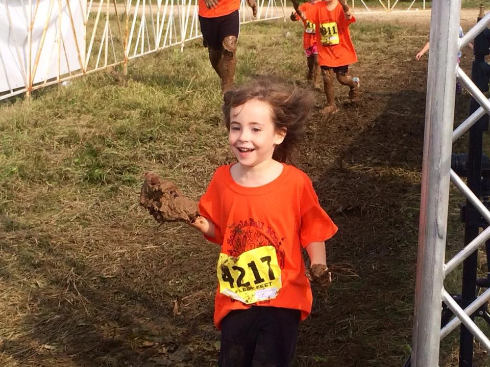 Aubree, Dr. Kaveh's, daughter crossing the finish line with a muddy shoe in hand but all smiles!