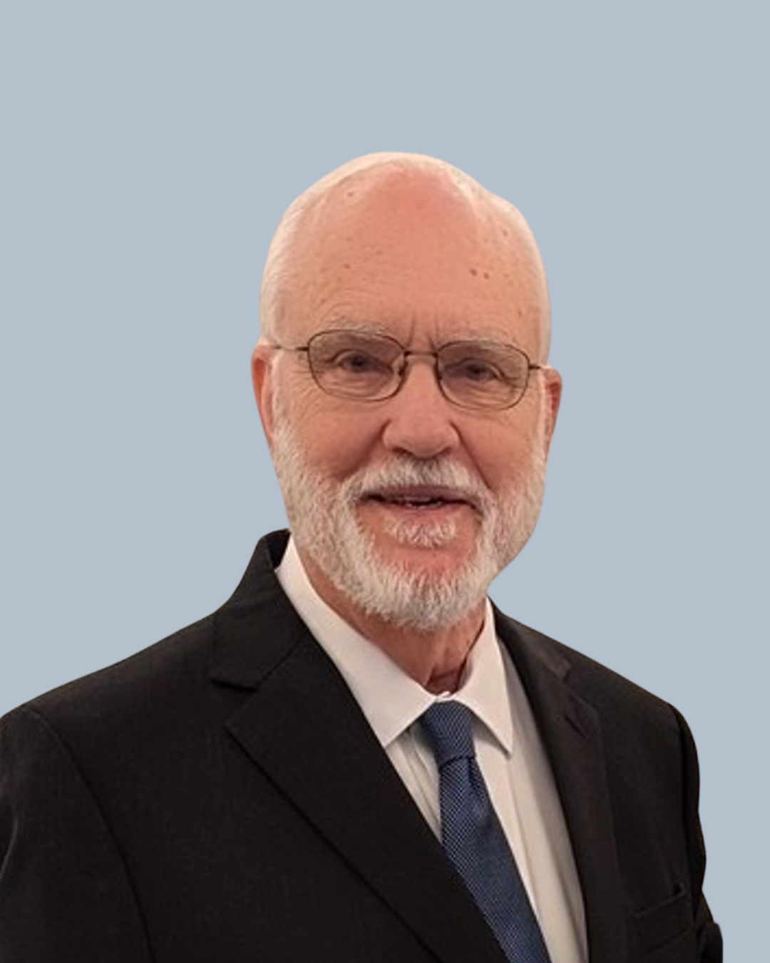 Portrait of elderly man with glasses, white beard, dressed in a black suit, white shirt, and blue tie, against a light blue background.