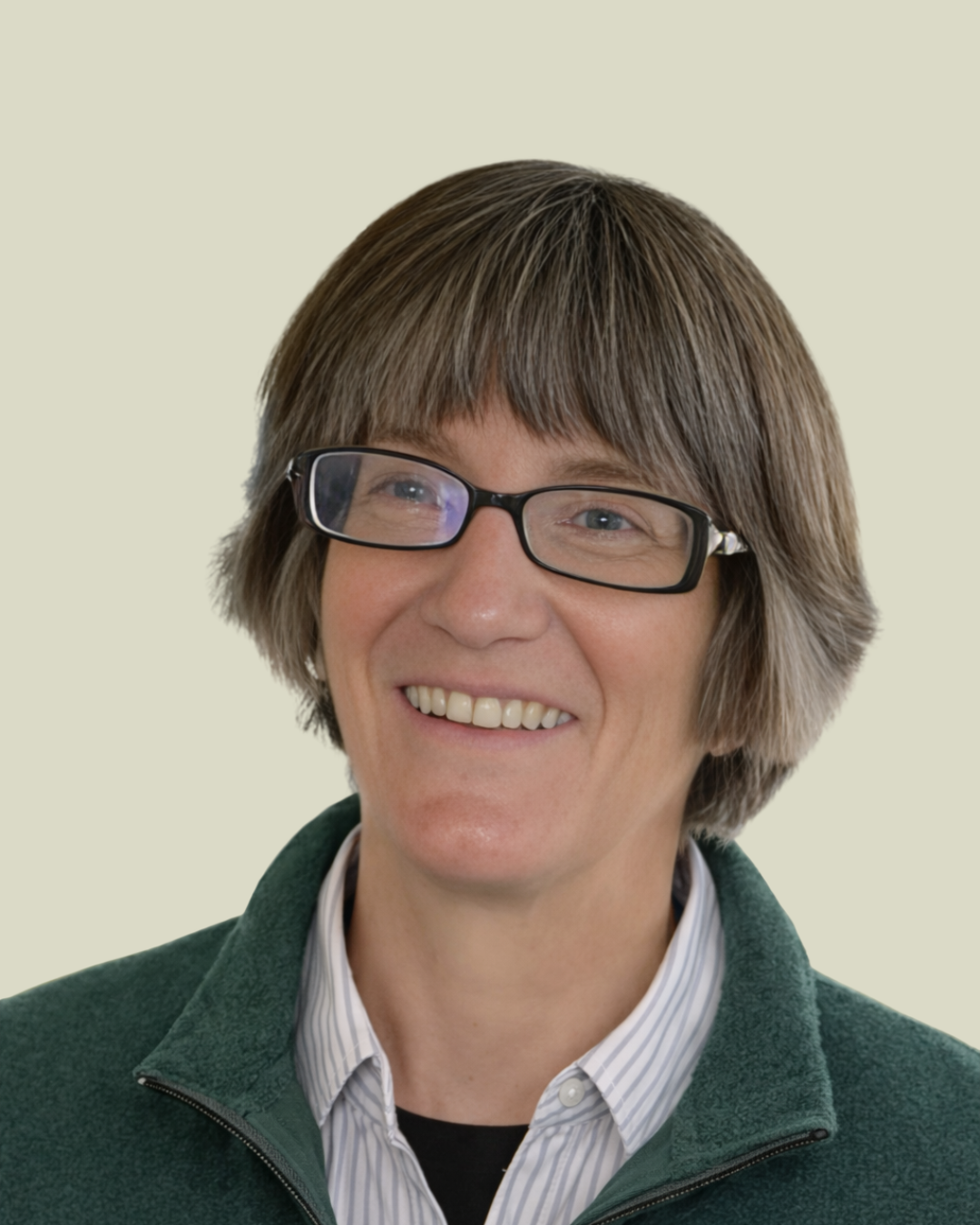 A woman with short brown hair wearing glasses, a collared shirt, and a green fleece jacket, smiling.