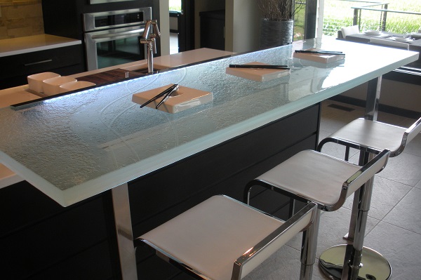 The above raised glass countertop features a custom surface texture, 1 ½” thickness, LED underlighting, and is being attached by a stainless steel bracket that is extending to the floor (stand -off brackets are also available which attach to the surface and not the floor)