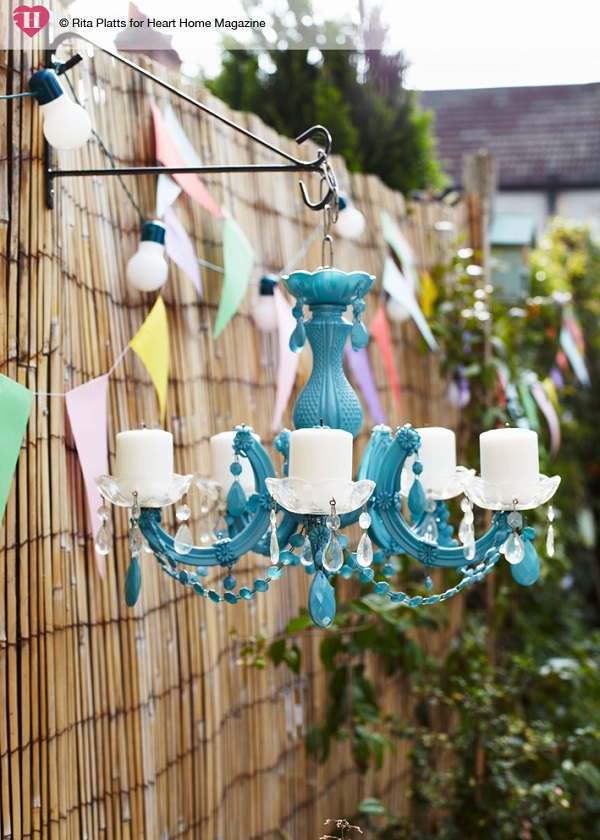 An old plastic chandelier, stripped of its wiring, creates a quirky, mood-setting outdoor light. Spray-painted a vibrant blue and with pillar candles added where light bulb fittings once were, it is hung from a hanging basket bracket screwed into a fence post.