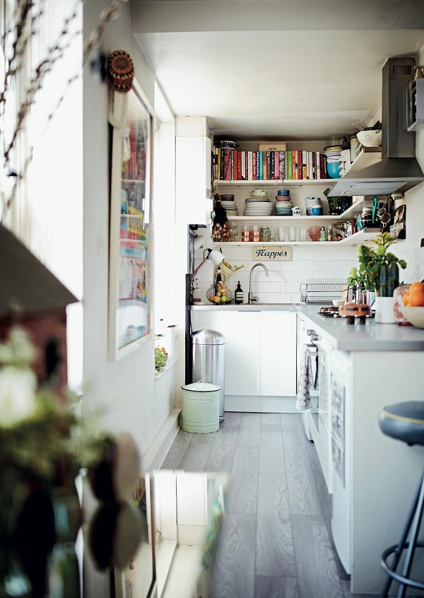 In the small galley kitchen just off the living room, storage is limited. Shelves are organised into cookbooks, pots/pans, dinnerware and glassware. A large framed poster hangs on the wall, adding further to the personality of the home.