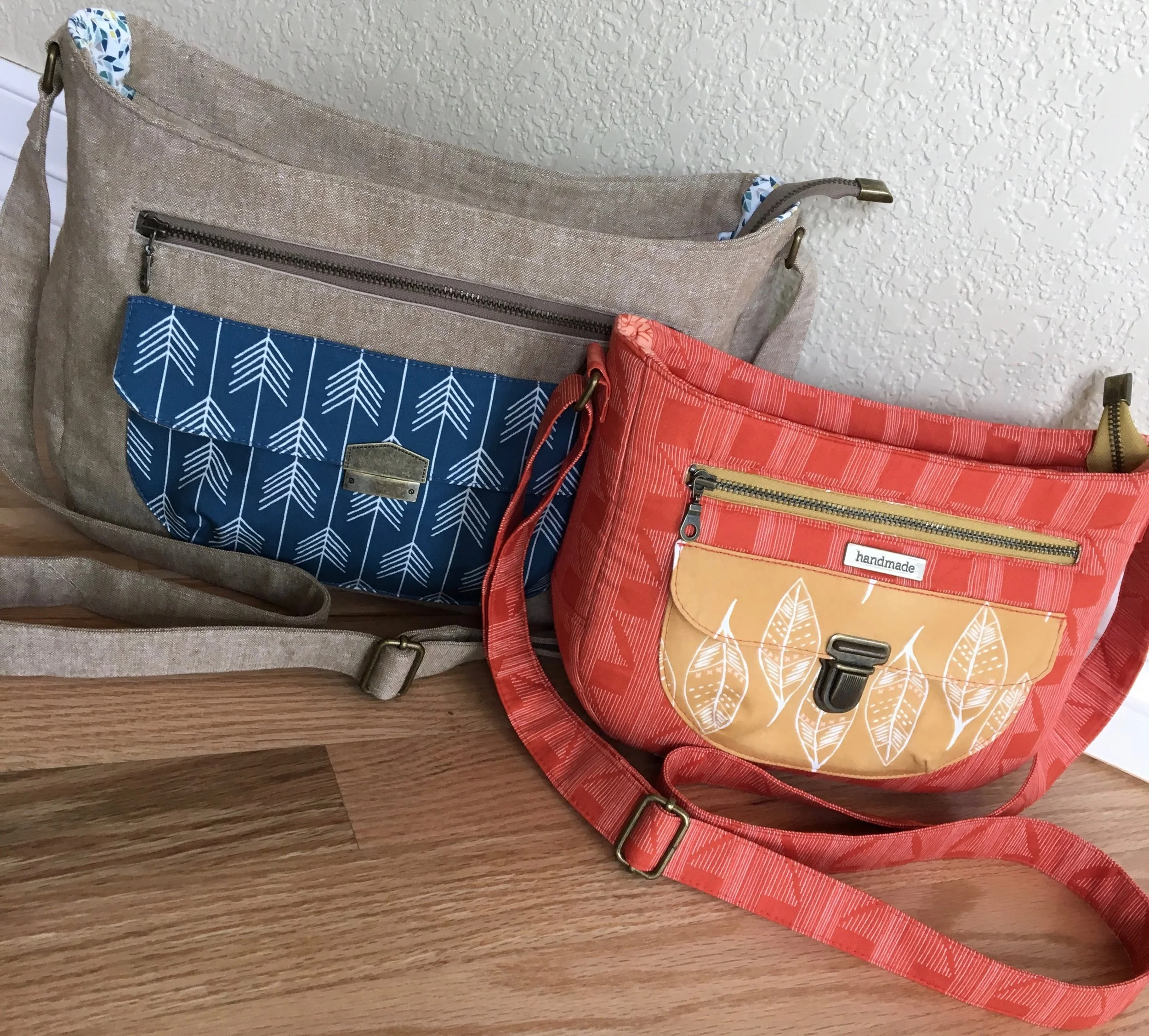The Aspen Crossbody Bag on the left is the large size - it has a "Snappy" Edge Clasp from Emmaline Bags for a pocket closure. The Aspen Crossbody Bag on the right is the small size. The small Aspen Crossbody has a Tongue Lock from Emmaline Bags for a pocket closure.