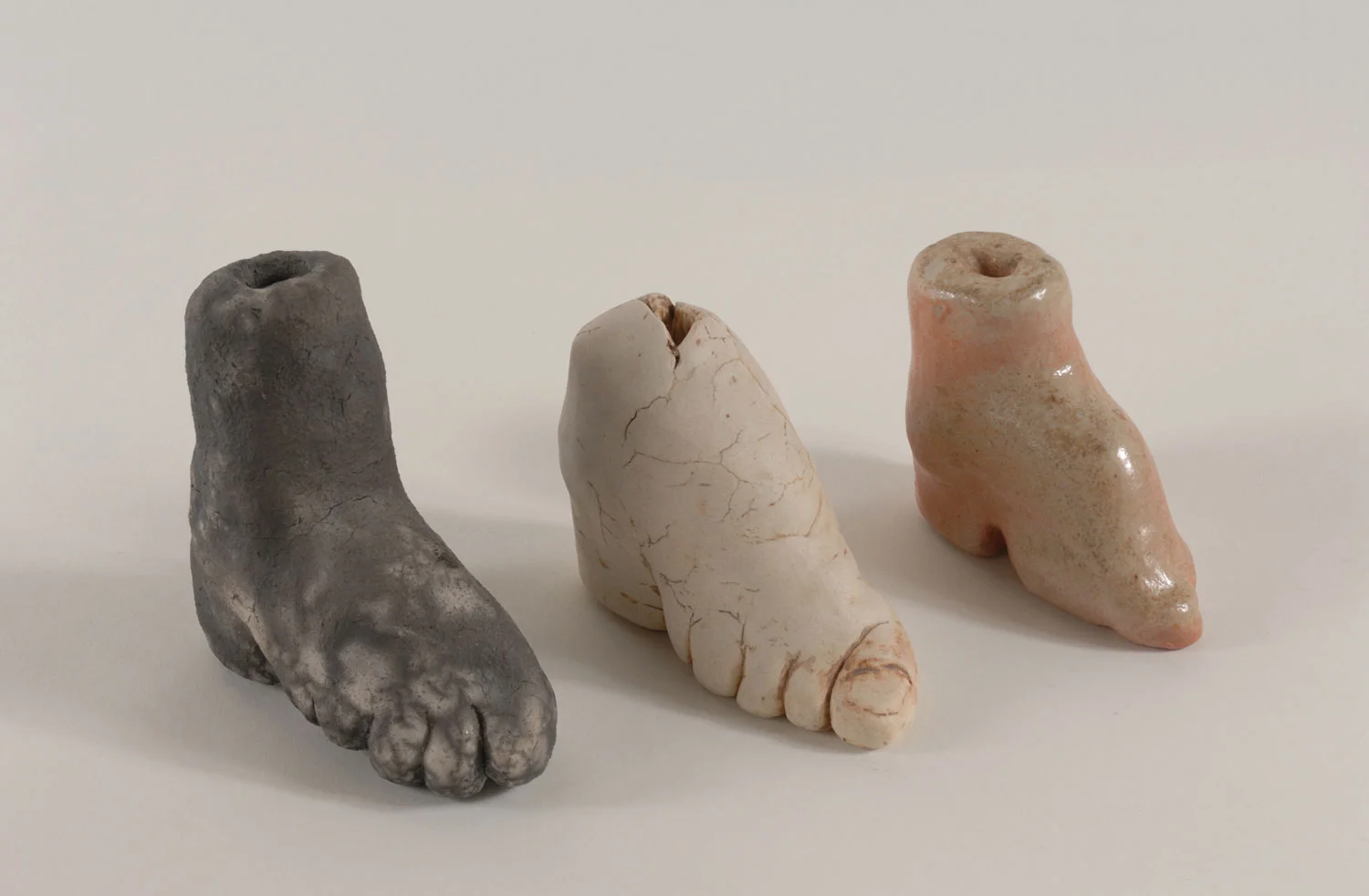 Three works from the Bound to Please series by Lorna Stevens depicting bound feet in Raku-fired, iron-washed, and wood-fired ceramic.