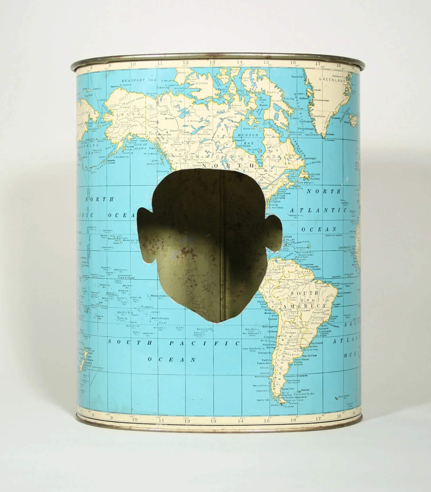 Waste, an artwork by Lorna Stevens made from a salvaged metal trashcan decorated with a world map, with a human face cut from its surface.