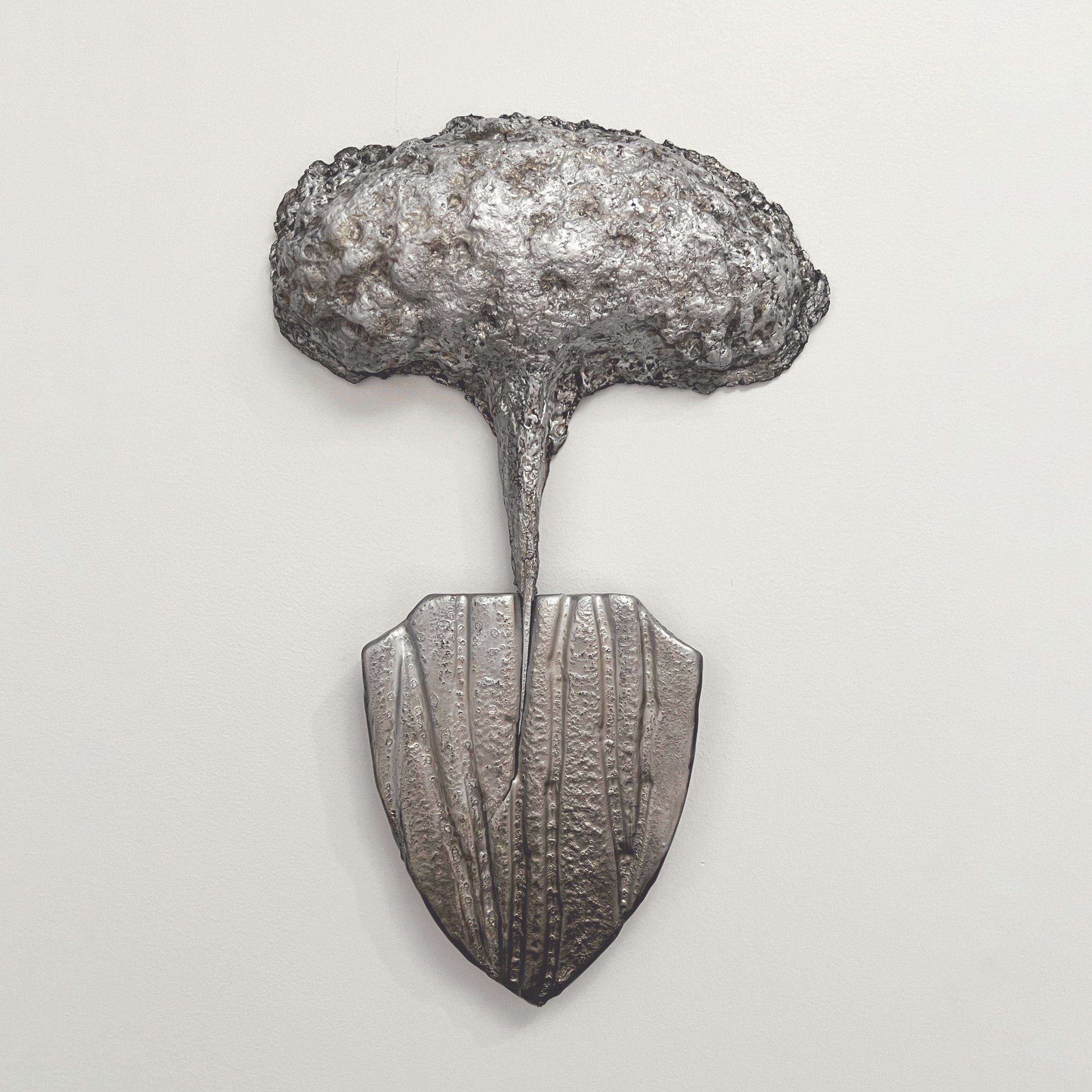 COVID, a shield-shaped wall-mounted artwork by Lorna Stevens made from cast paper, ceramic, and spray paint.