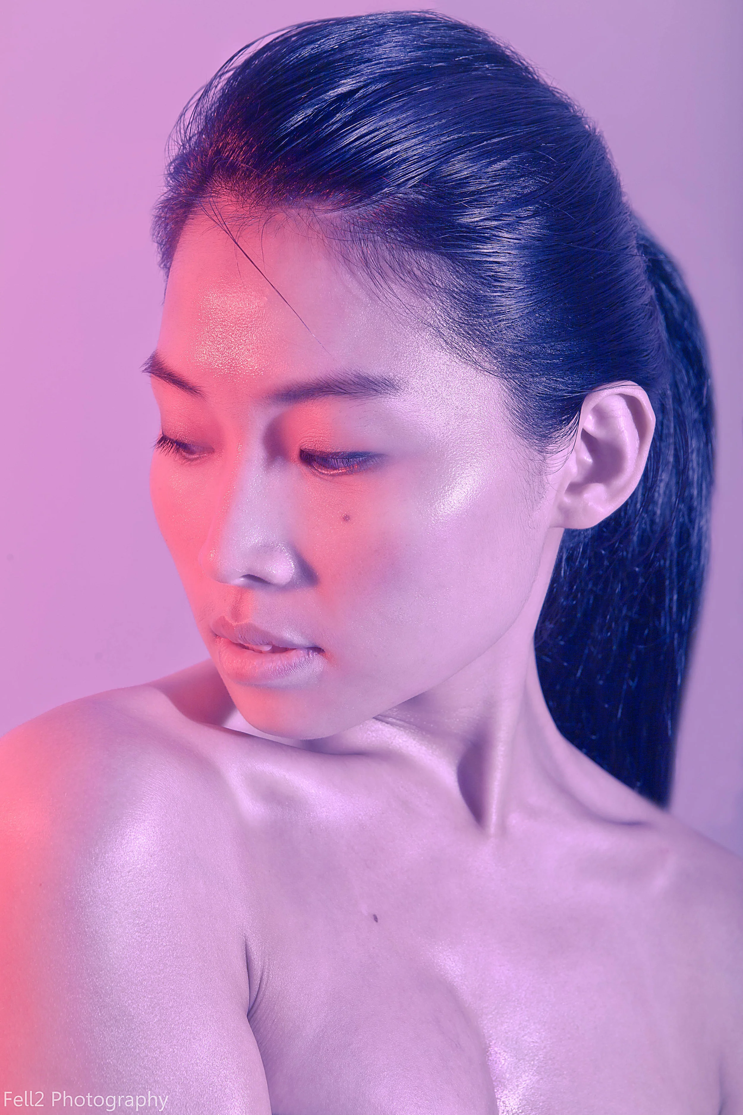 Close-up of a woman with closed eyes and long, dark hair styled back, illuminated with pink and purple lighting.