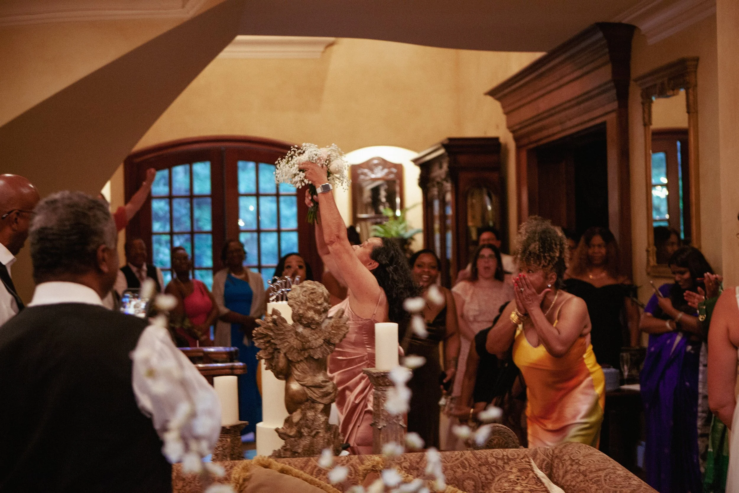 Woman celebrating at a birthday party with a cake and a flock of white feathers falling, surrounded by onlookers in a warmly lit room.