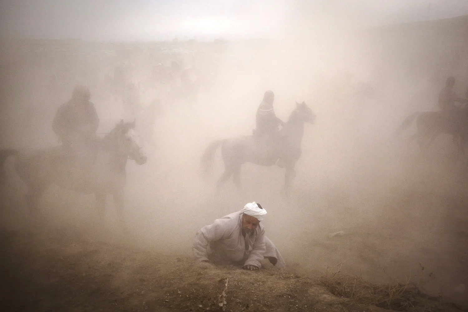 Too slow to jump to a retreat with the rest of the audience, an old man is lost in the dust of a horde of buzkashi horses. Near Sharinav, Tajikistan. Popular throughout much of Central Asia, buzkashi is a form of horse polo in which horseback players wrestle a goat carcass across a playing field.