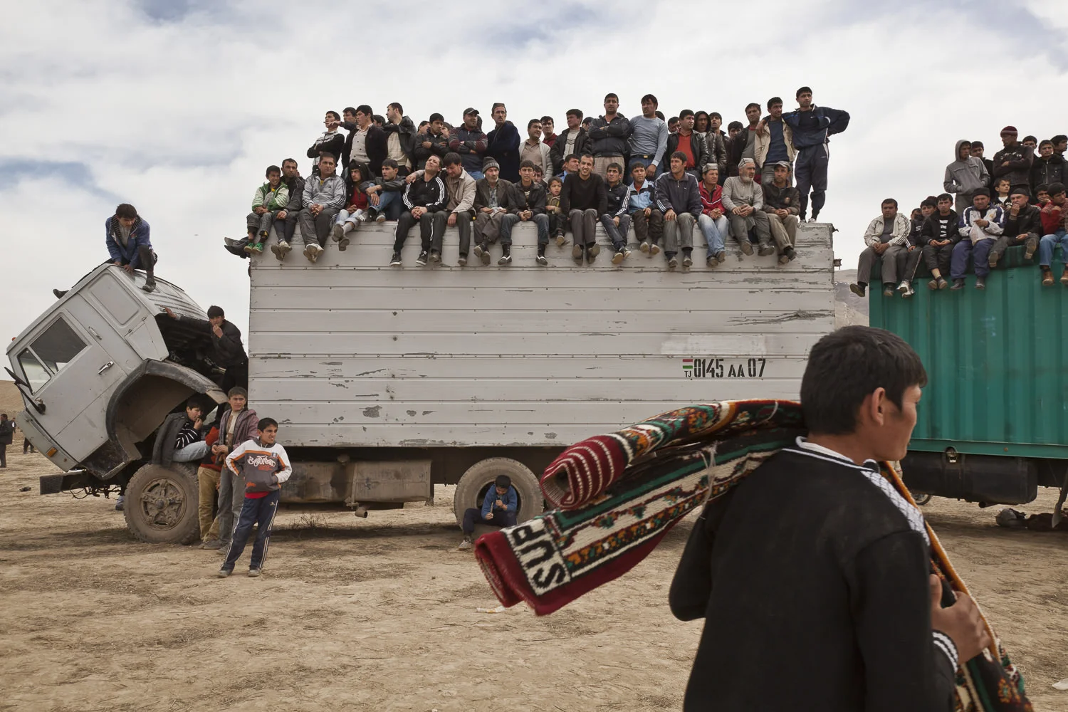 Spectators look on from a high perch on top of trucks, as a chovandoz assistant carries away a carpet won as a prize during the match in Hisor, western Tajikistan.