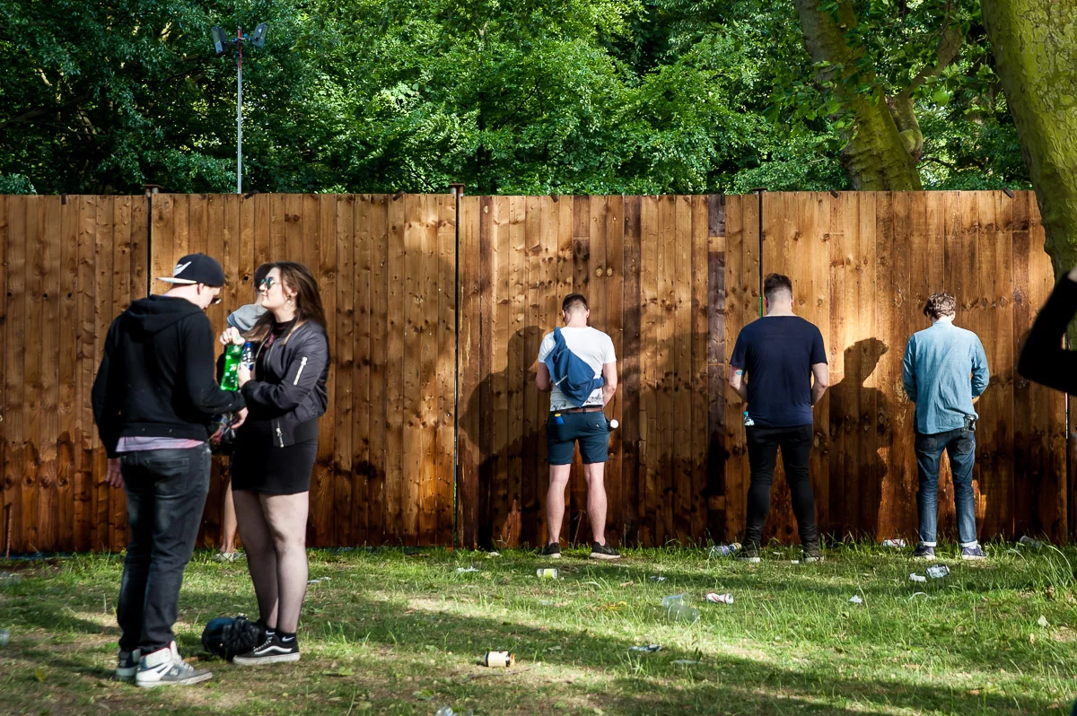Male festival goers pissing on a wooden fence, Field Day, Victoria Park, London, UK, 06/06/2015 © Dosfotos