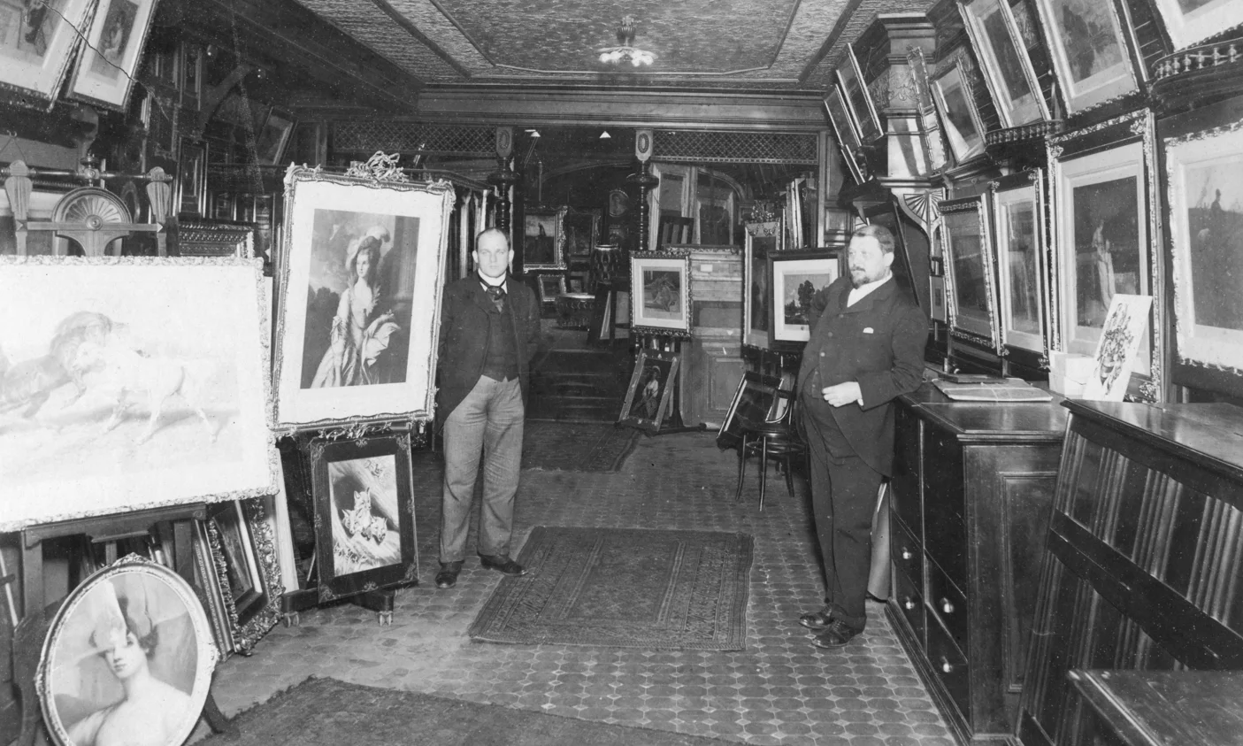 Black and white photo of Charles and John Kraushaar in front of framed art