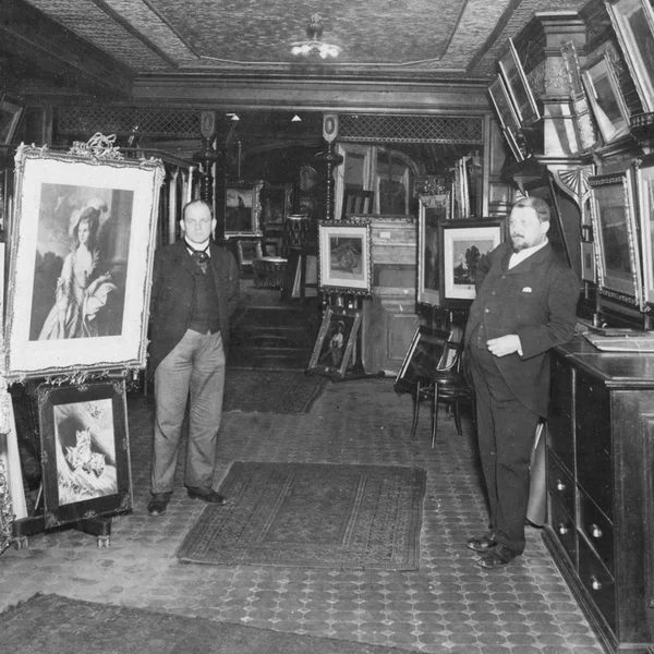 Black and white photo of Charles and John Kraushaar in front of framed art