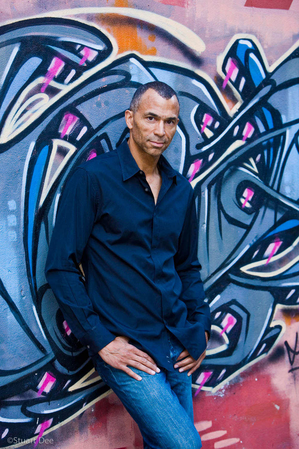 Man in front of a wall spray-painted with grafitti.