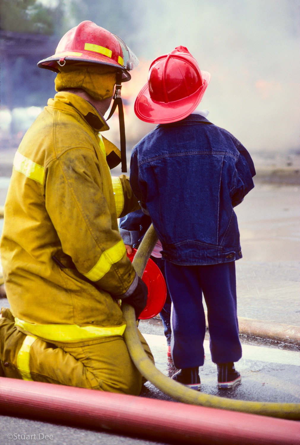  Young boy watching a fireman keep fire under control 