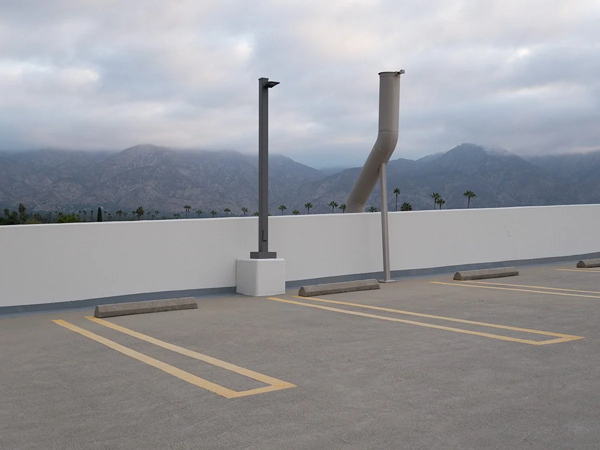  Deck Studies explores the elevated, empty top decks of urban parking structures across Pasadena, California. Positioned above the street level, these utilitarian concrete spaces serve as quiet vantage points and visual sanctuaries—letting the adjace