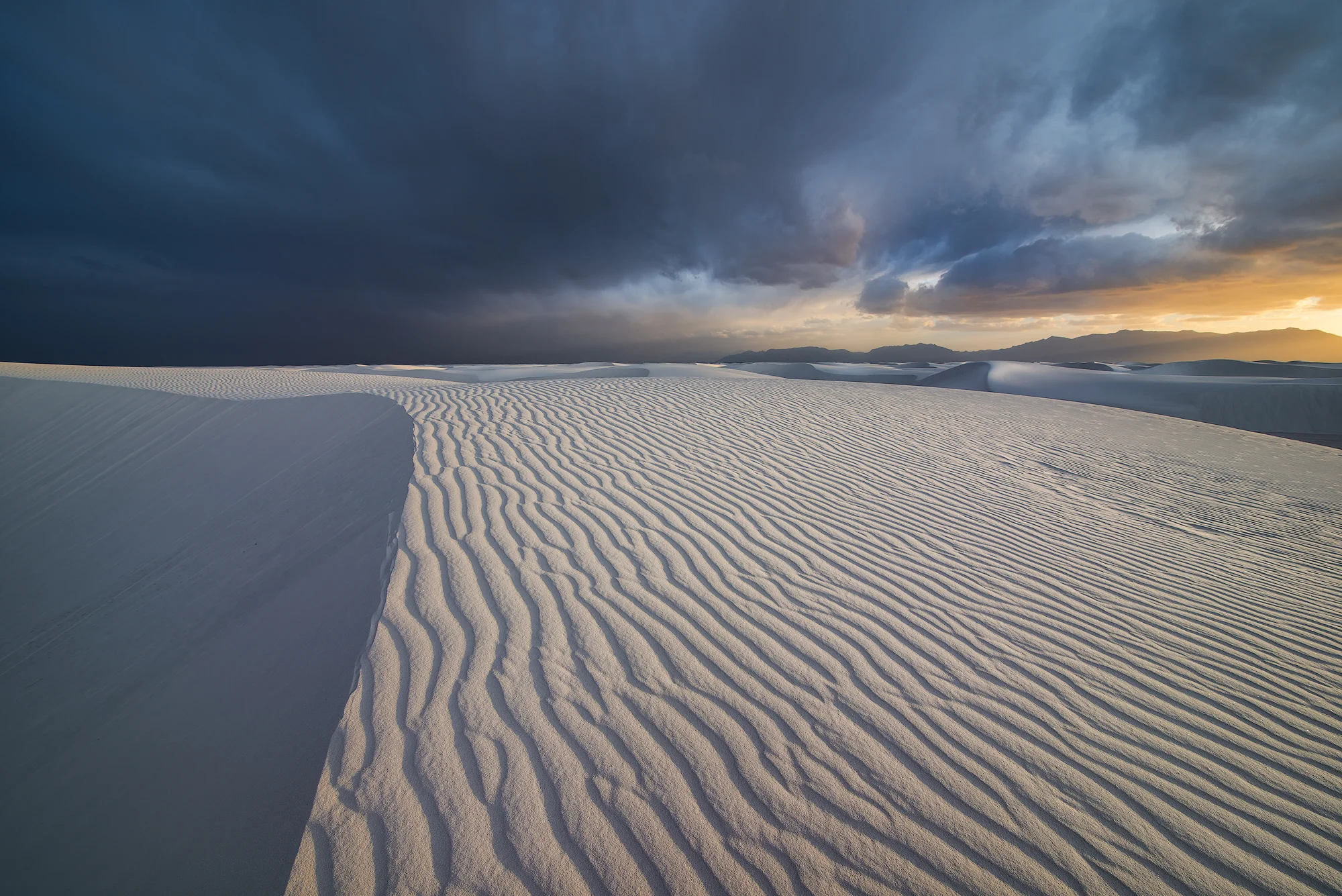 Storm clouds break near sunset send beautiful light across a rippled sand dune.