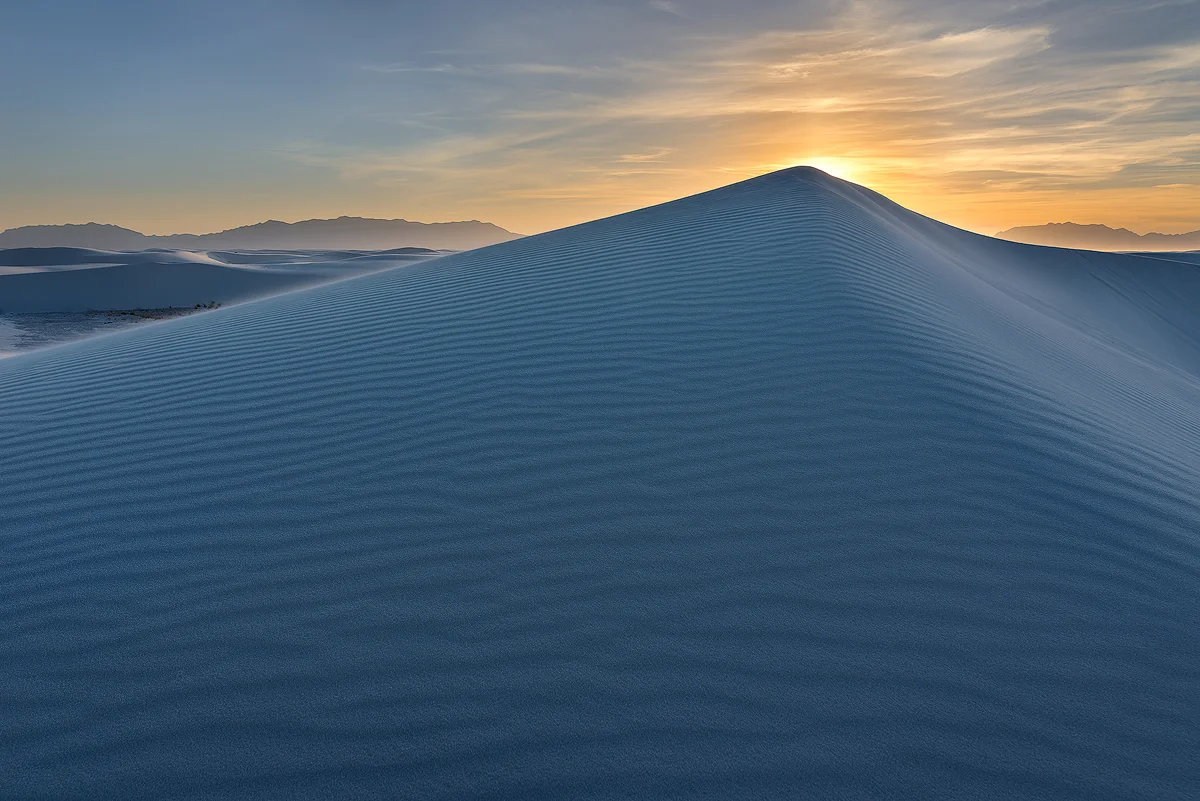 The beautiful gold tones of sunset offset the blue light and shadows of a pyramidal sand dune.