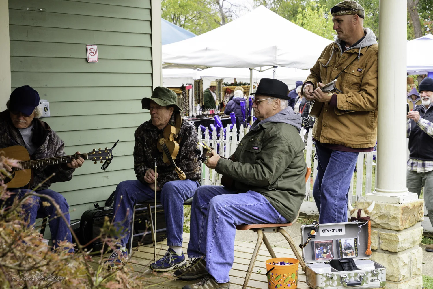 I have observed some rules about porch jamming. You don't need to know anyone on the porch. Show up with your instrument, determine if you can play the songs at the level of performance of the group and then wait for an empty chair. If anyone leaves and you are at the front of the line you can take a seat and just join in. The gentleman standing on the left is at the front of the line and he is already playing. The complement of instruments does not seem to matter. There is no such thing as too many guitars or not enough violins.
